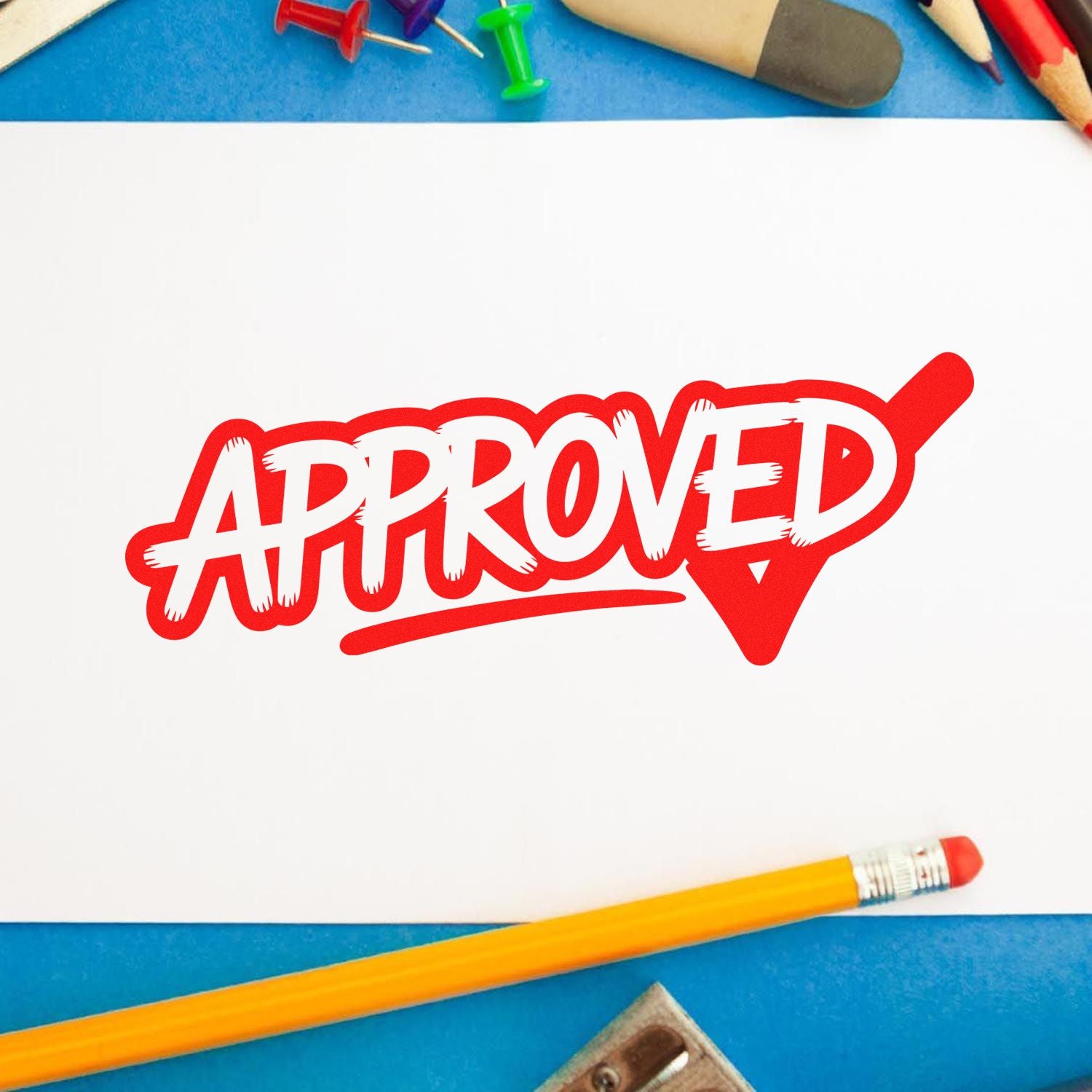 Red APPROVED stamp seal on white paper, with blue background, pencils, and push pins.