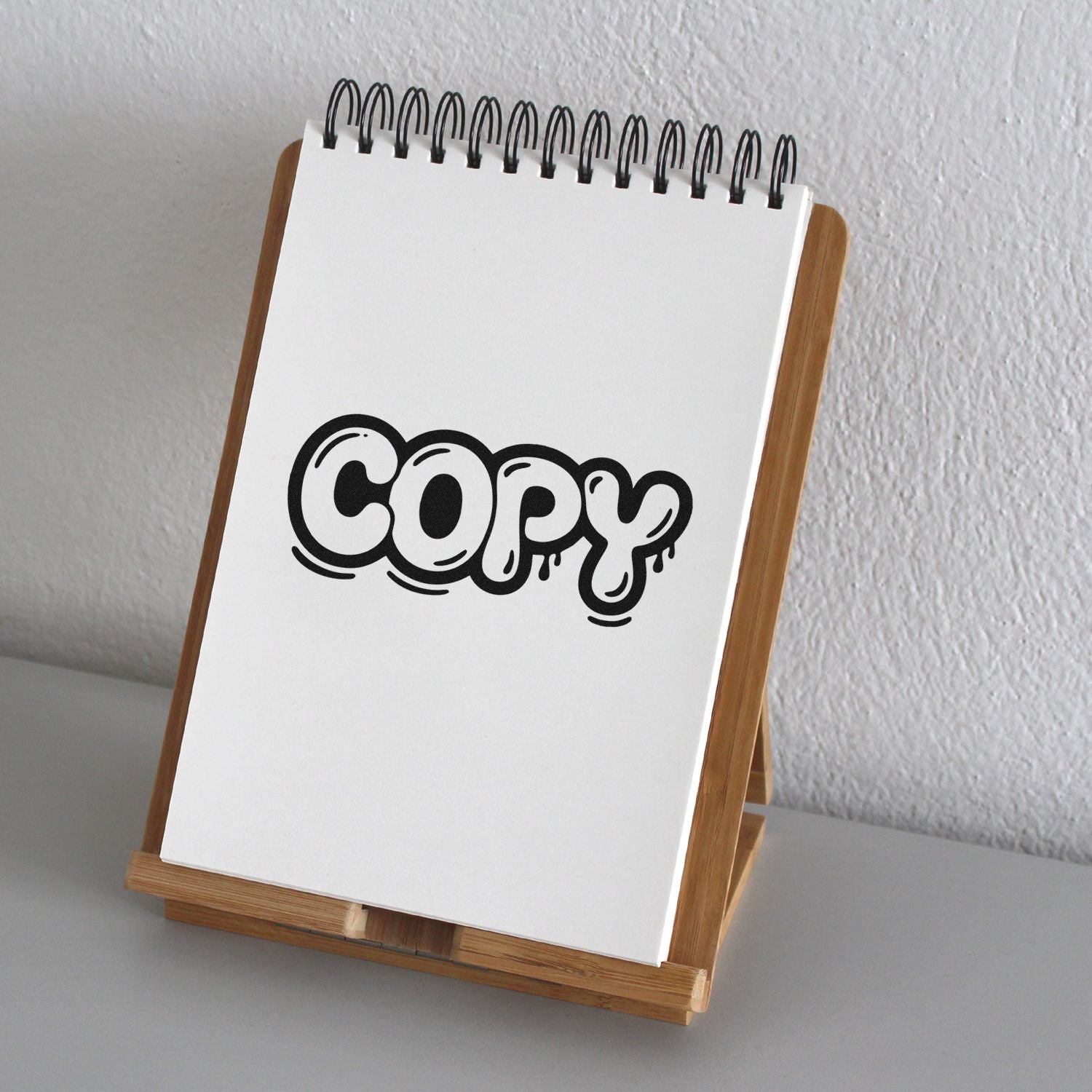 Black copy stamp and seal design on a white spiral notepad displayed on a wooden easel.