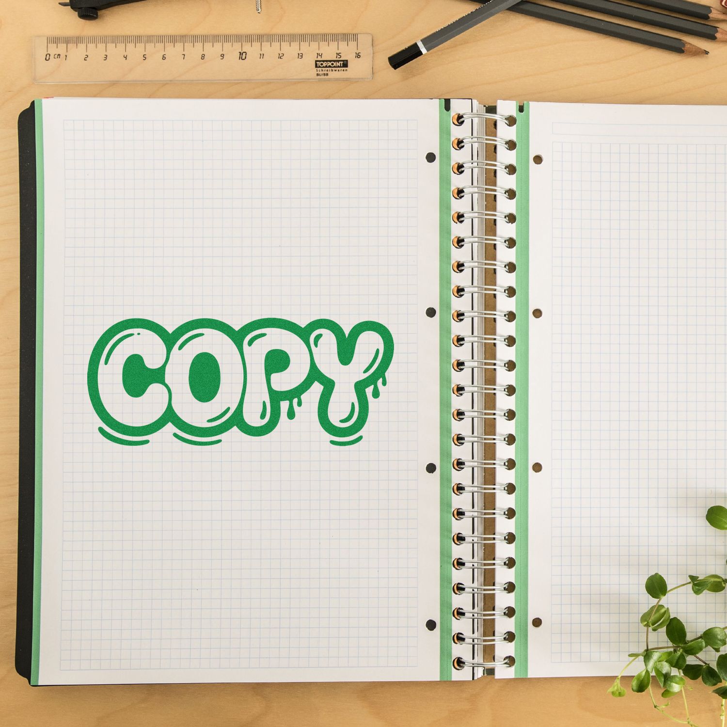 Green COPY stamp seal on graph paper notebook beside spiral binding, ruler, and pencils on a wooden desk.