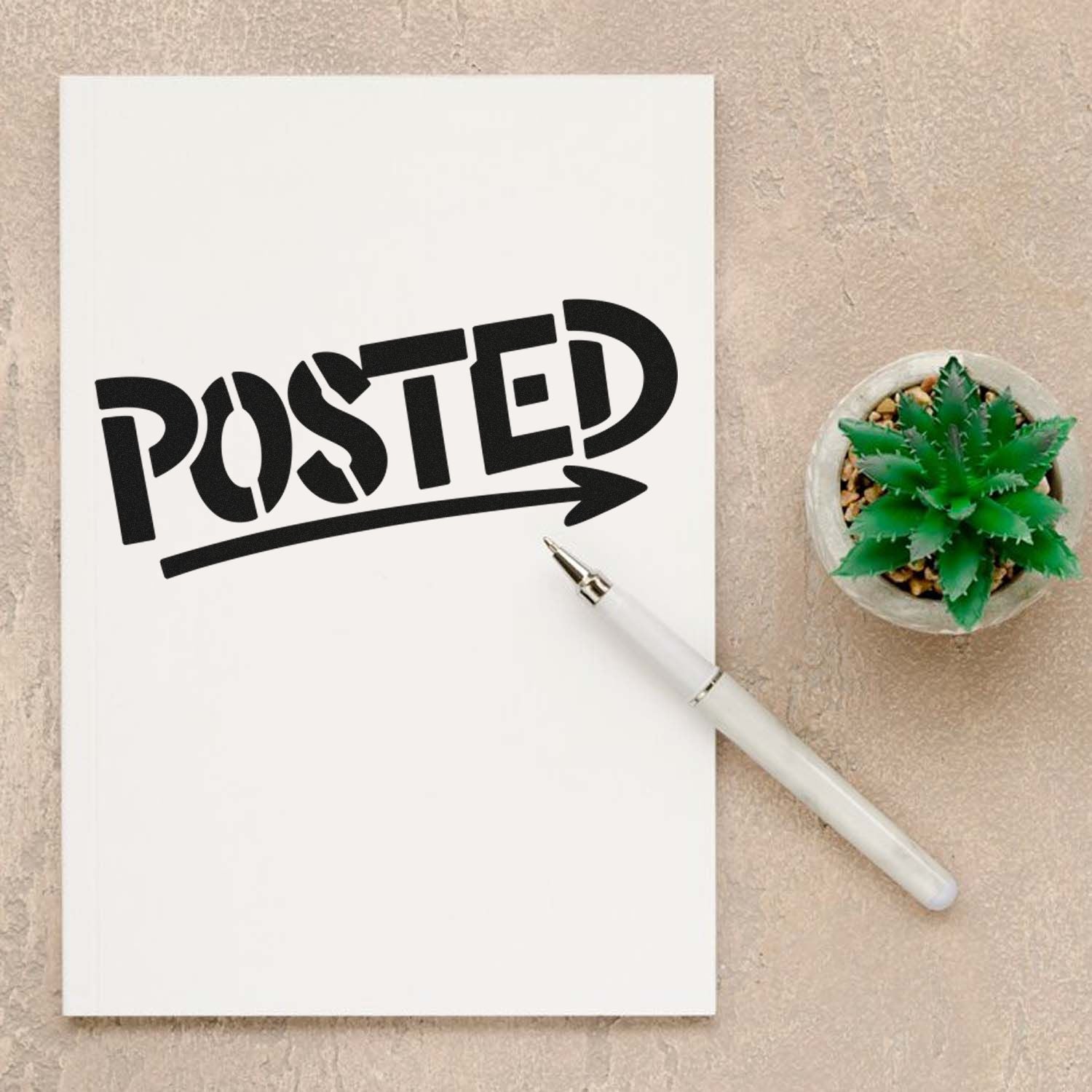 Black POSTED rubber stamp on white paper, with white pen and green succulent on a beige background