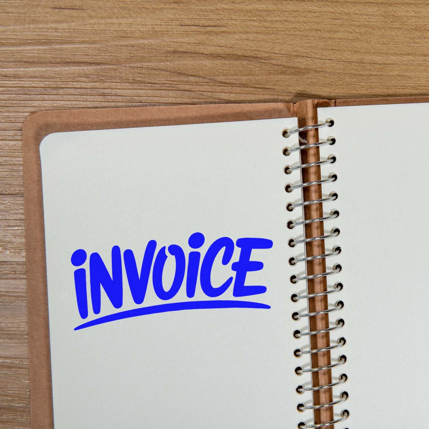 Blue invoice stamp/seal on a white spiral notebook page, with brown cover and wood desk background.