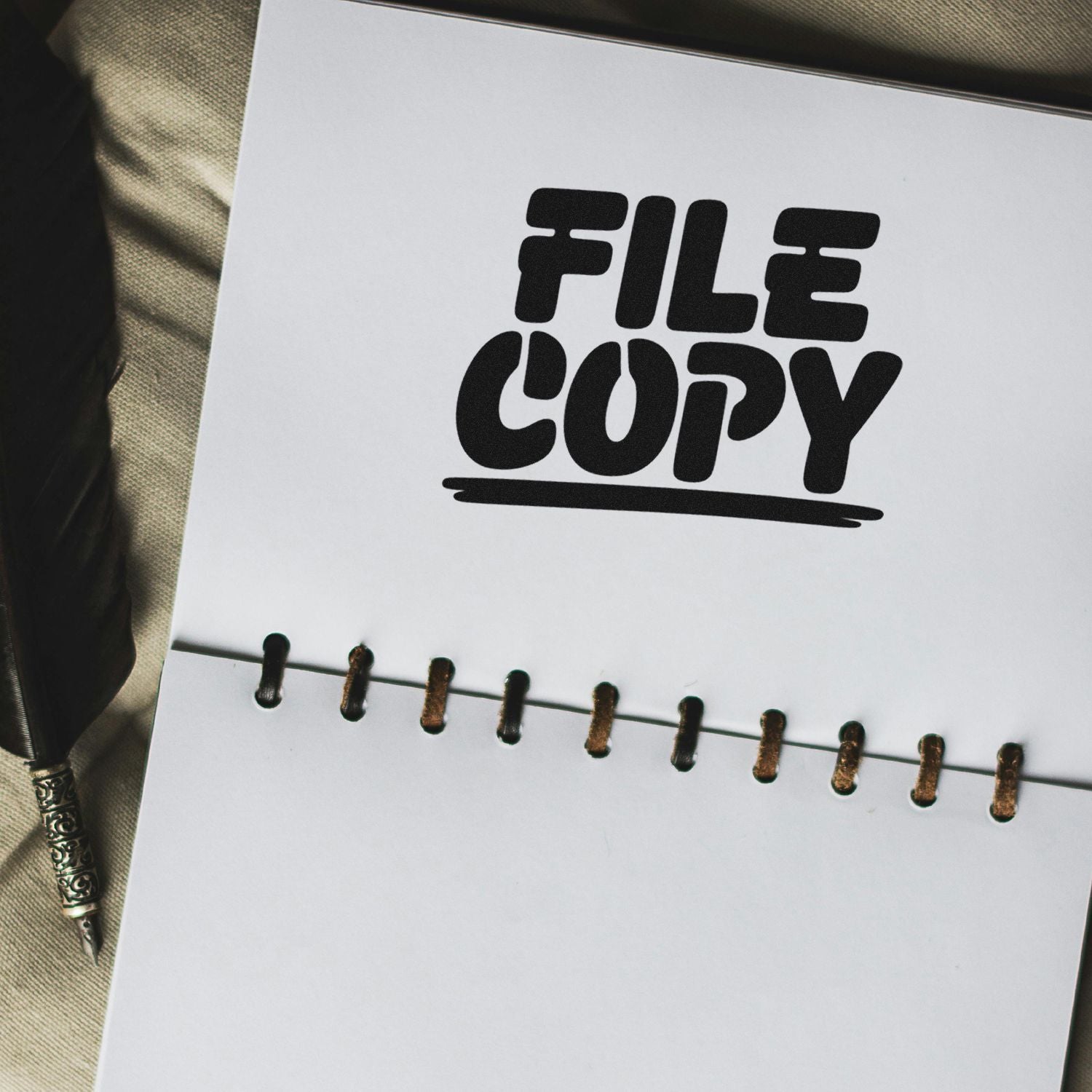 Black FILE COPY rubber stamp on white spiral-bound paper, with brass binding and pen beside it.