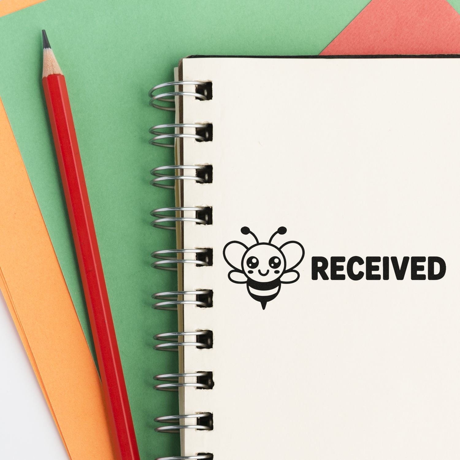 Notebook page with black RECEIVED stamp and bee seal icon, beside a red pencil on green, orange, and pink paper.