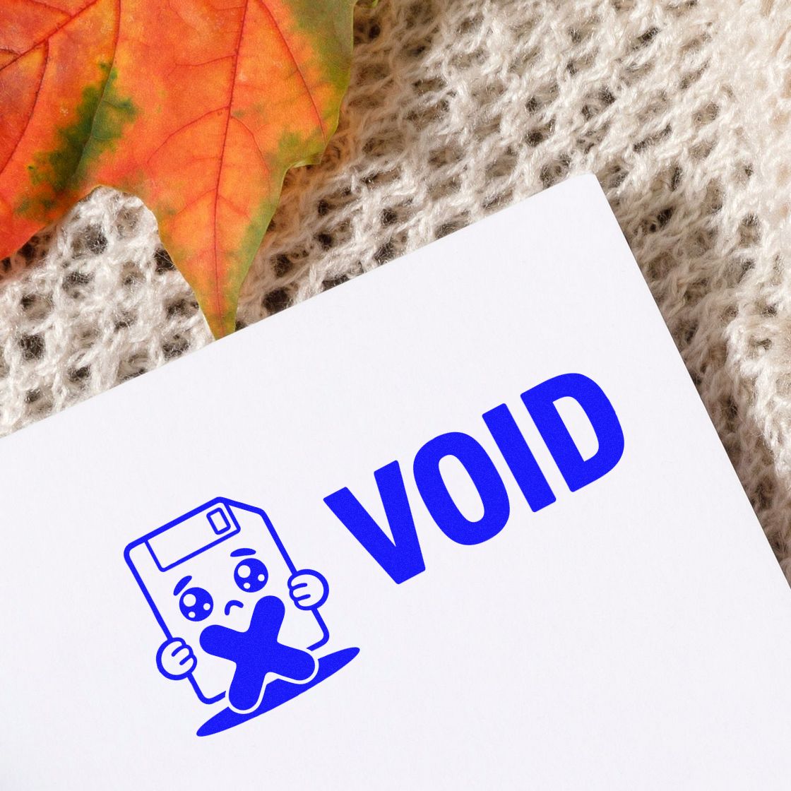 Blue VOID tamper-evident stamp seal on white paper, with a blue mascot icon, beige knit background, and orange leaf.