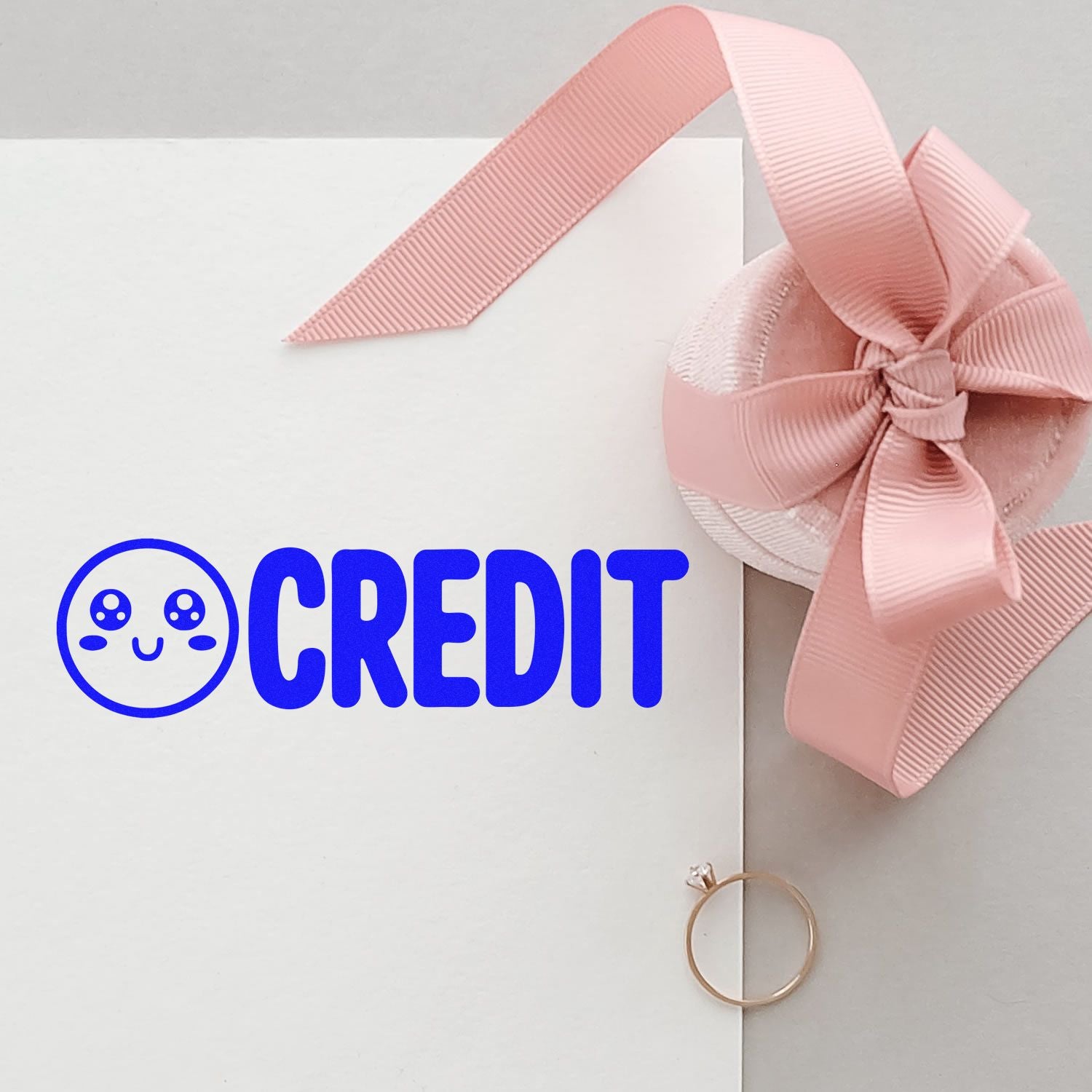 White stamp and seal box with blue CREDIT logo, pink ribbon bow seal, and gold ring embellishment