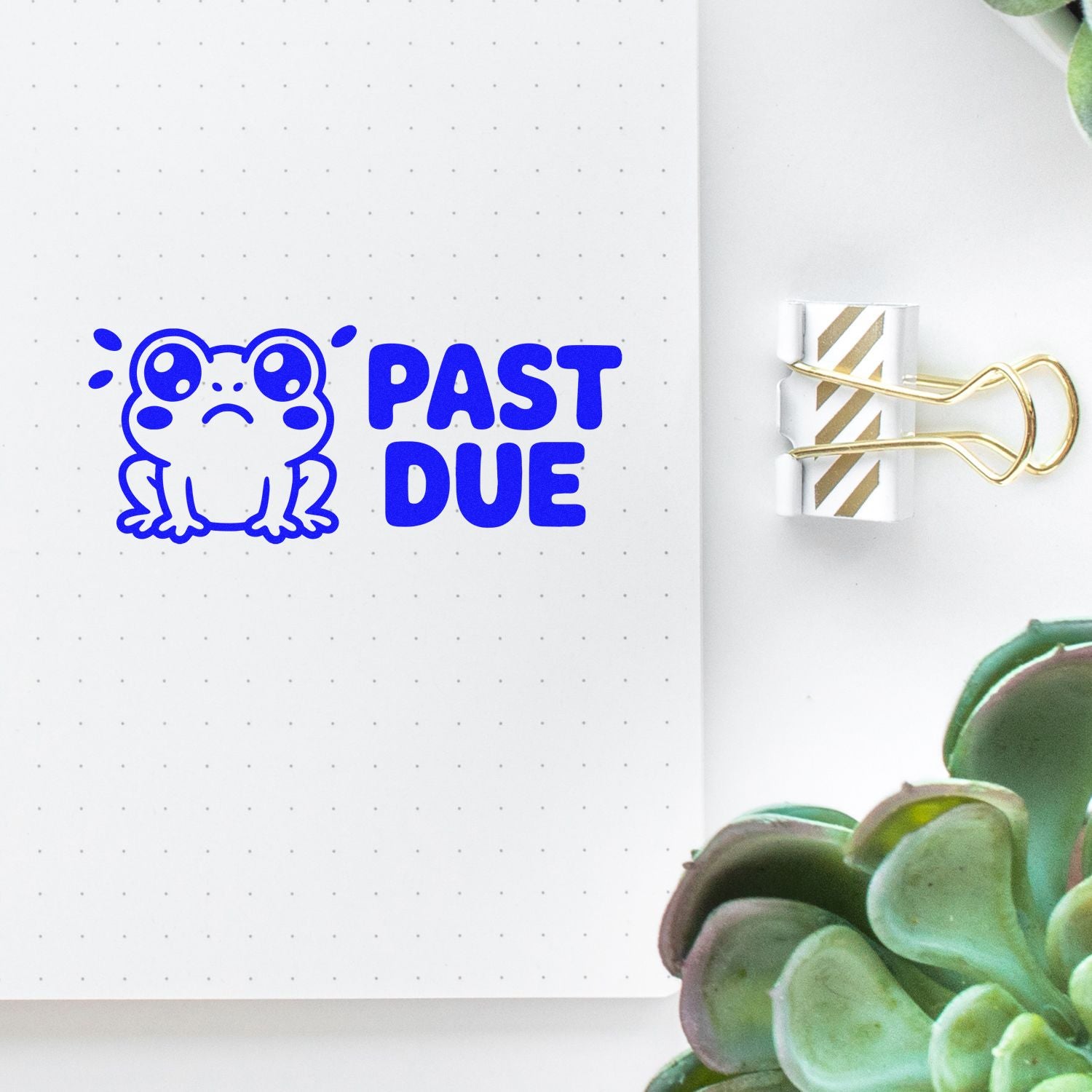 Blue PAST DUE frog stamp and gold-striped binder clip seal on dotted notebook page, with green succulent.
