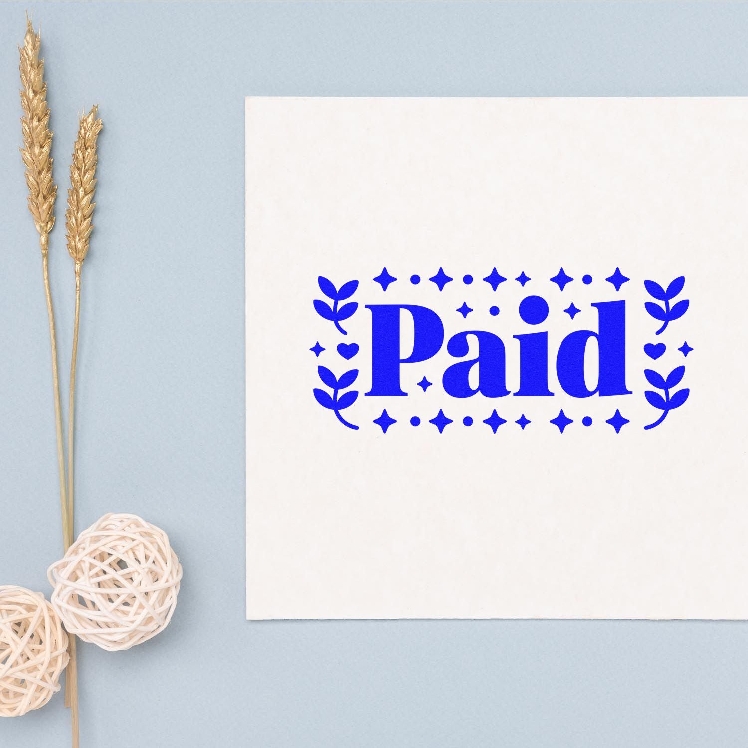 Blue Paid stamp seal on white card with stars and leaves, on light blue background beside dried wheat and woven balls.