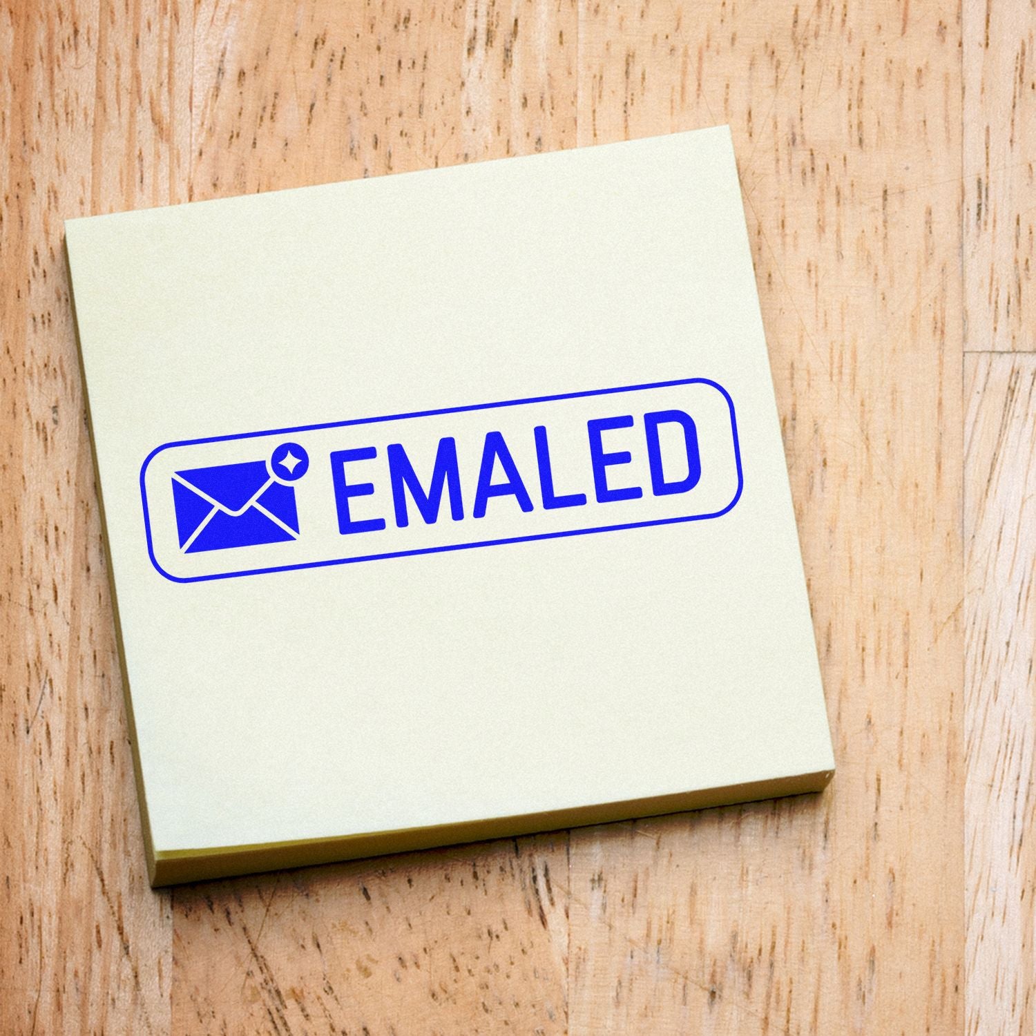 Blue EMAILED rubber stamp seal with envelope icon on cream note pad over wood surface.