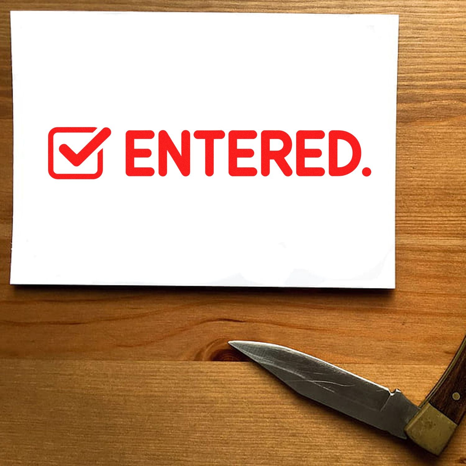 Red ENTERED stamp and checkmark seal on white card over a wood tabletop.