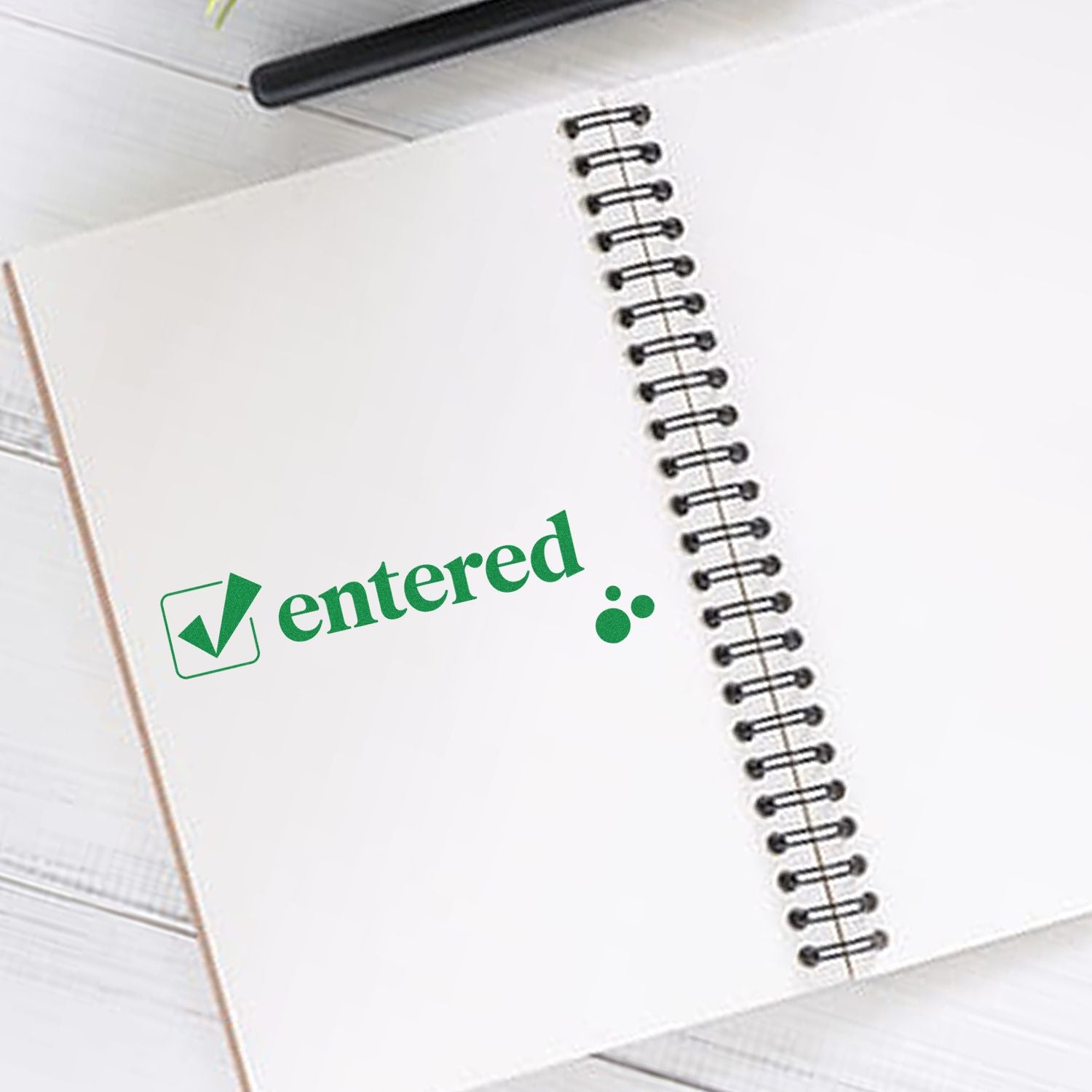 Green entered stamp seal with checkmark on a white spiral notebook.