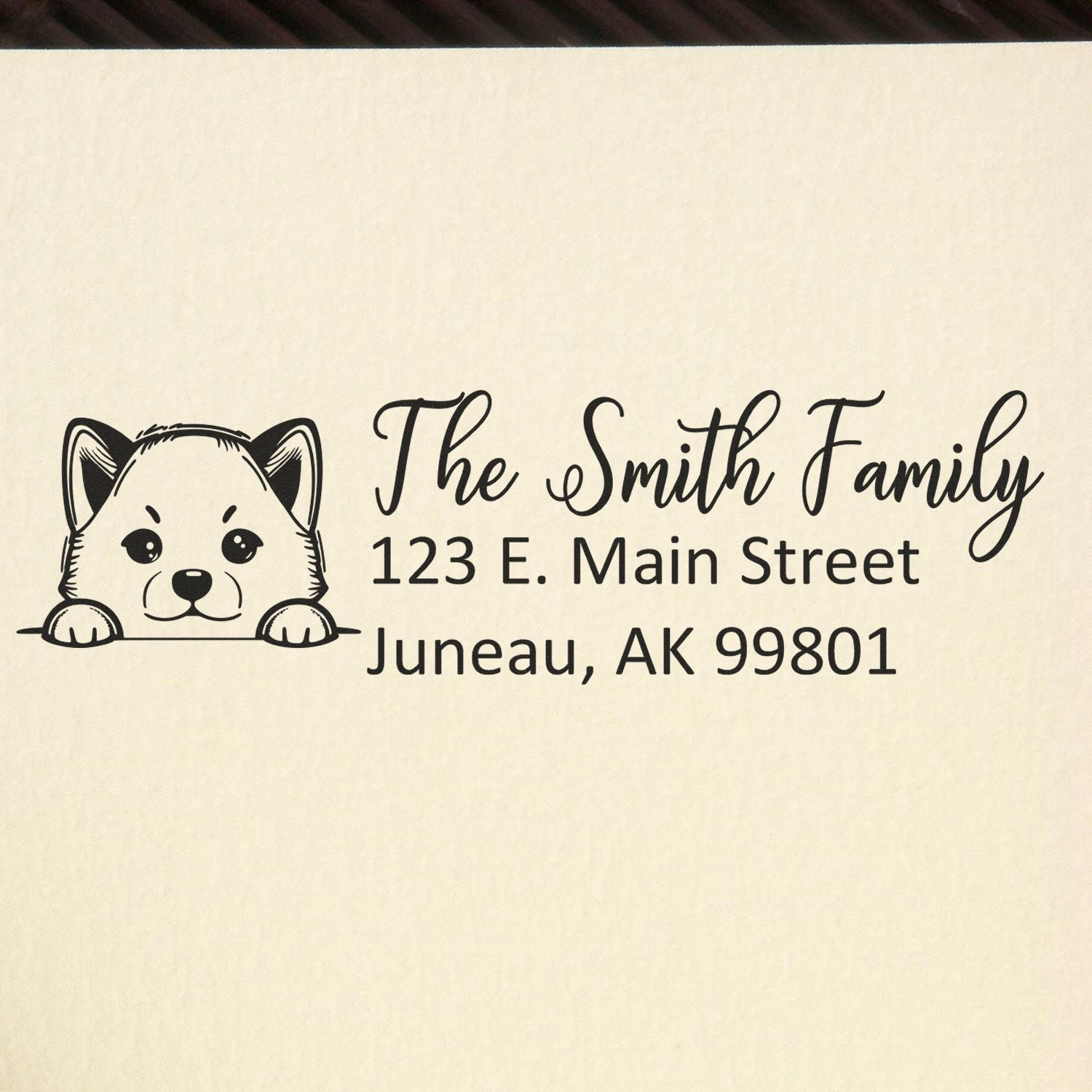 Black personalized address stamp with cute dog seal icon, reading The Smith Family, 123 E. Main Street, Juneau, AK 99801 on cream paper.