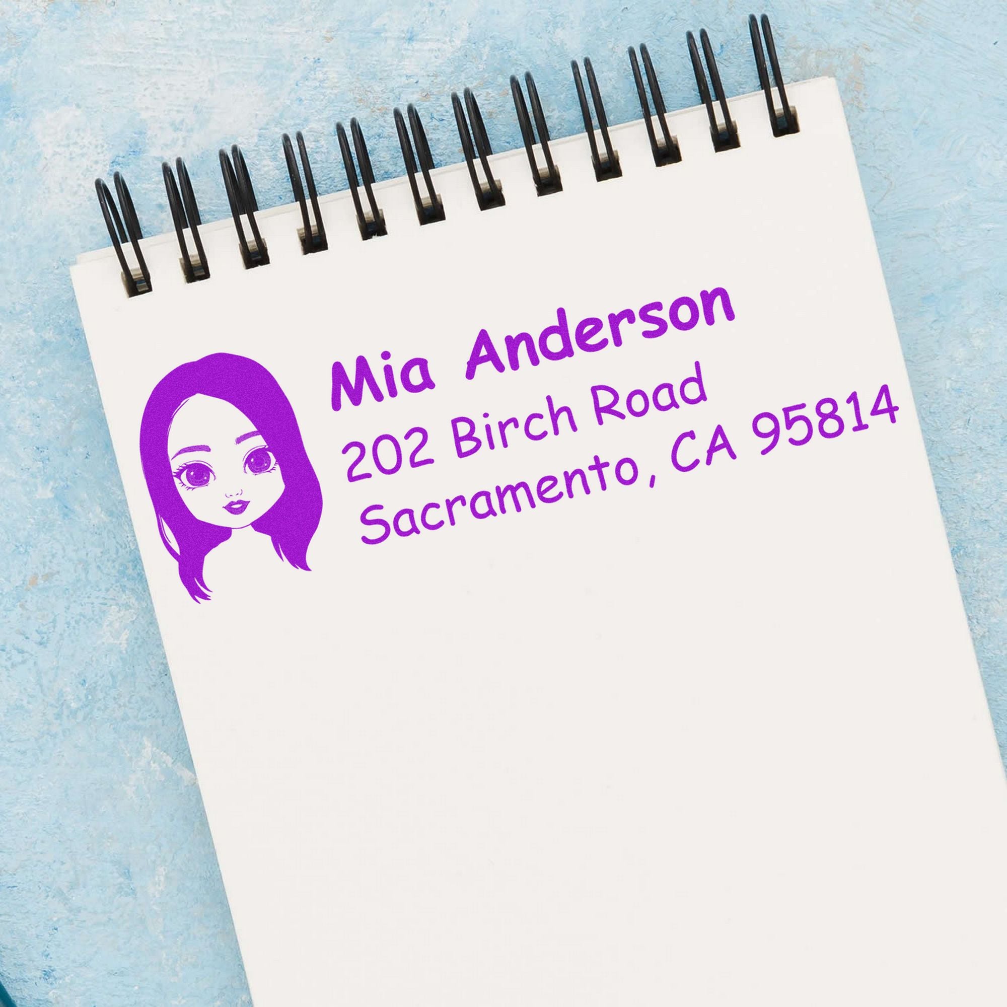 Purple custom address stamp and seal on a white spiral notepad, showing a female avatar and Mia Anderson Sacramento address on blue background.