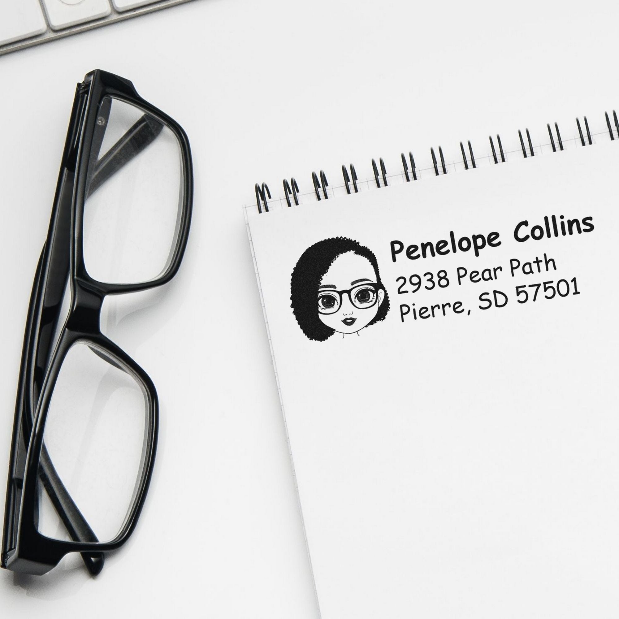 Black eyeglasses beside a white custom self-inking address stamp and seal with cartoon logo and black text.