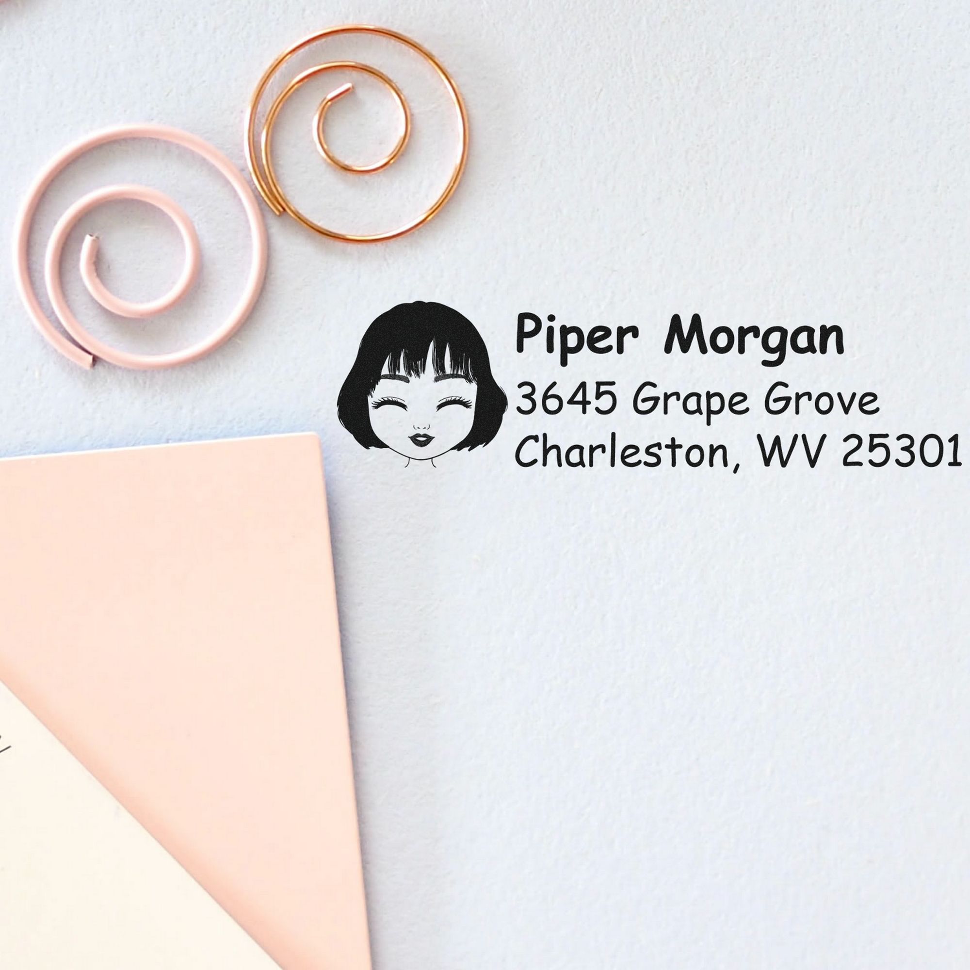 Personalized black return address stamp with girl logo, beside pink and gold spiral wax seal stamps on white paper.