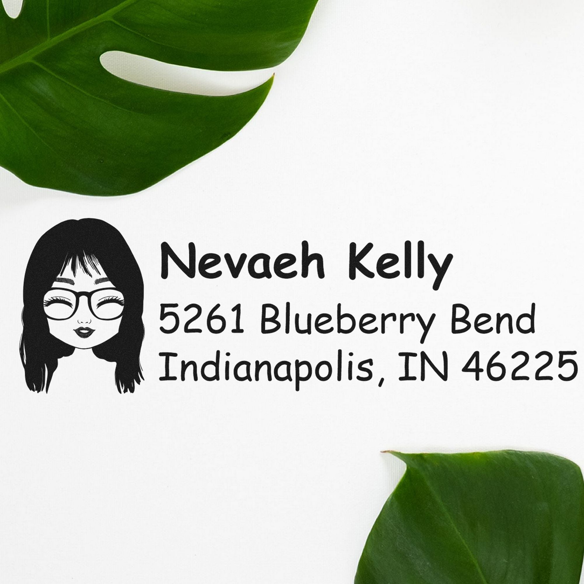Black custom address stamp and seal with cartoon face logo, Nevaeh Kelly, and Indianapolis IN 46225 on white, framed by green leaves.