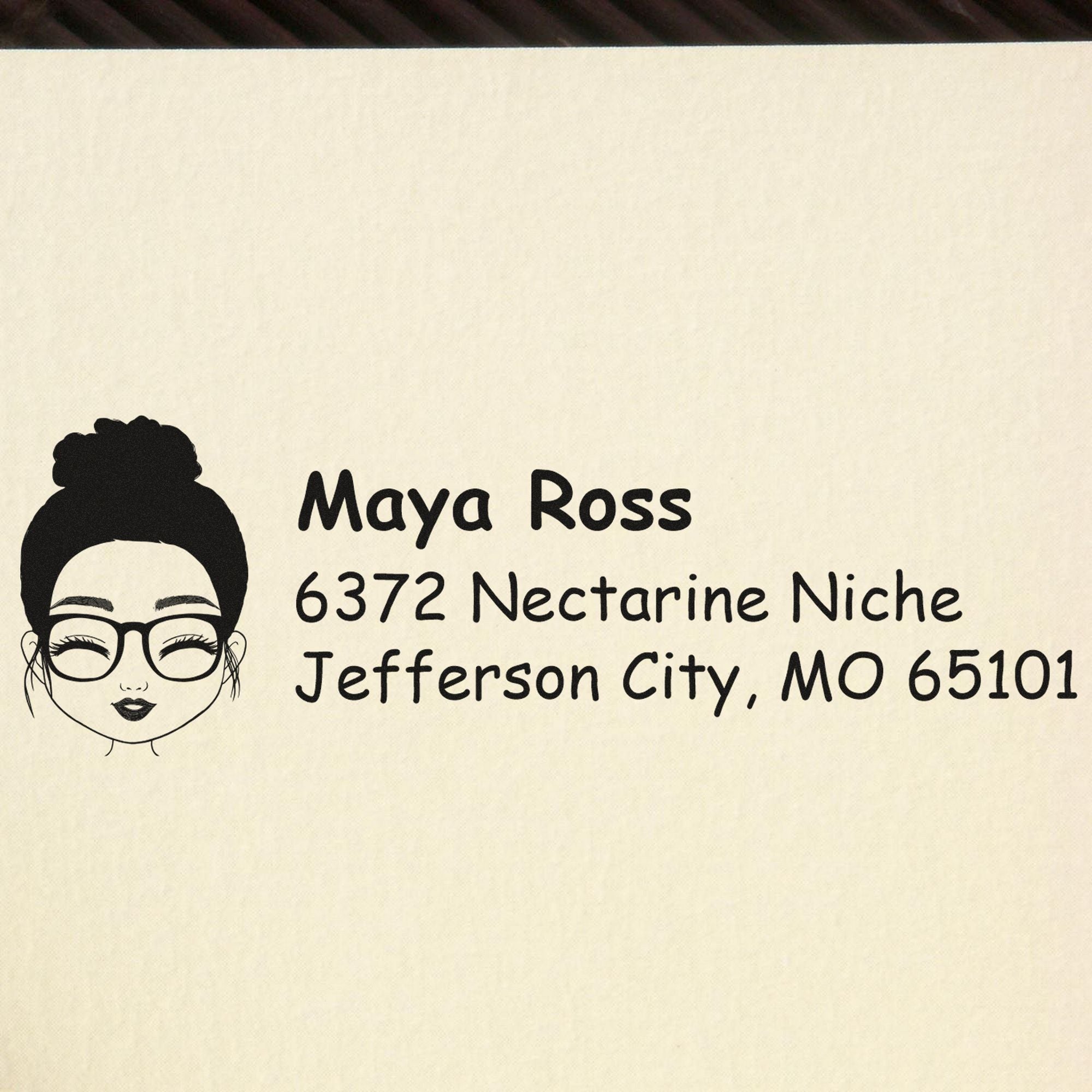 Black custom address stamp with woman avatar on cream paper, reading Maya Ross, 6372 Nectarine Niche, Jefferson City, MO 65101