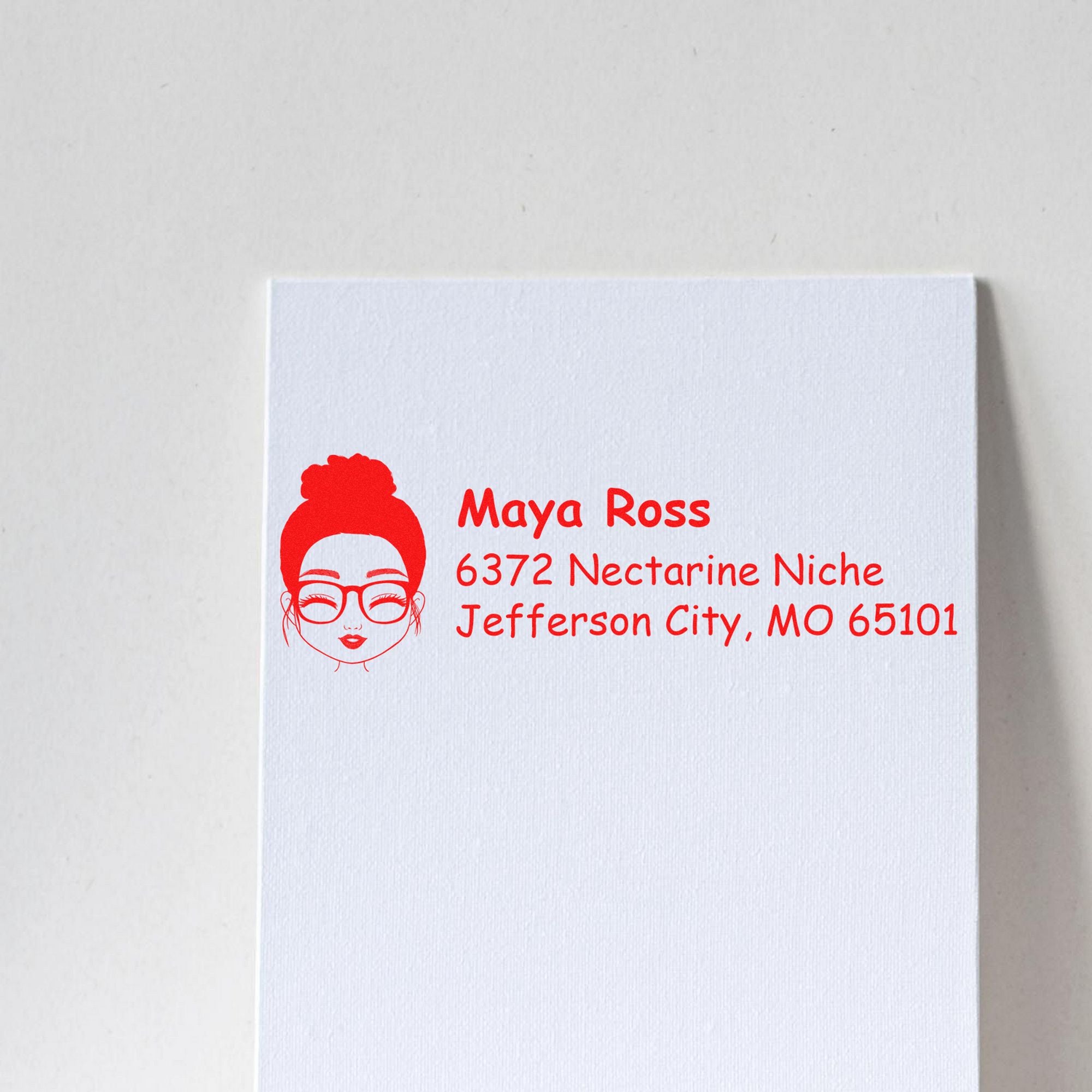 Red custom address stamp and seal with face logo, Maya Ross address on white paper