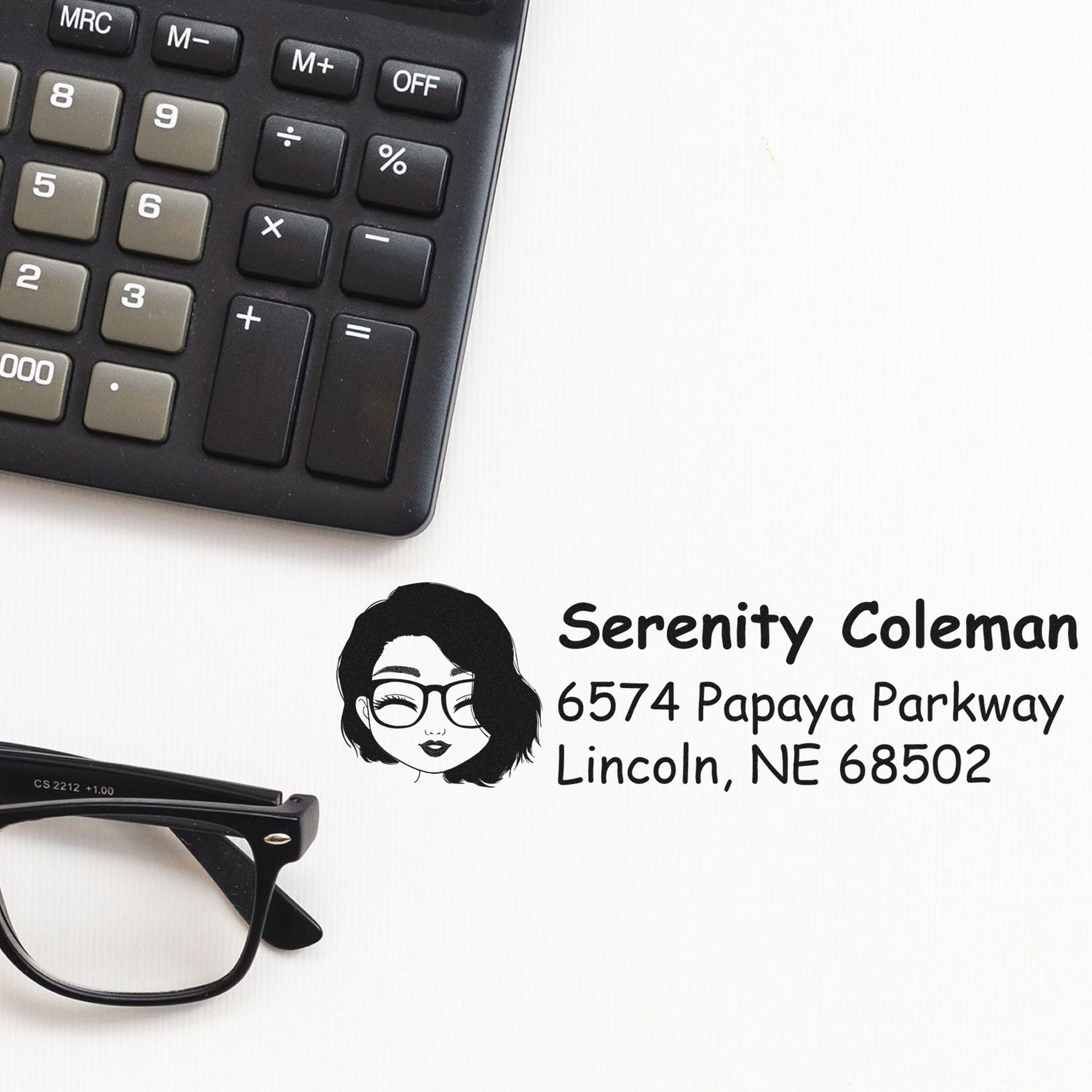 Black self-inking stamp and seal with name and address, shown beside a calculator and eyeglasses on a white background.