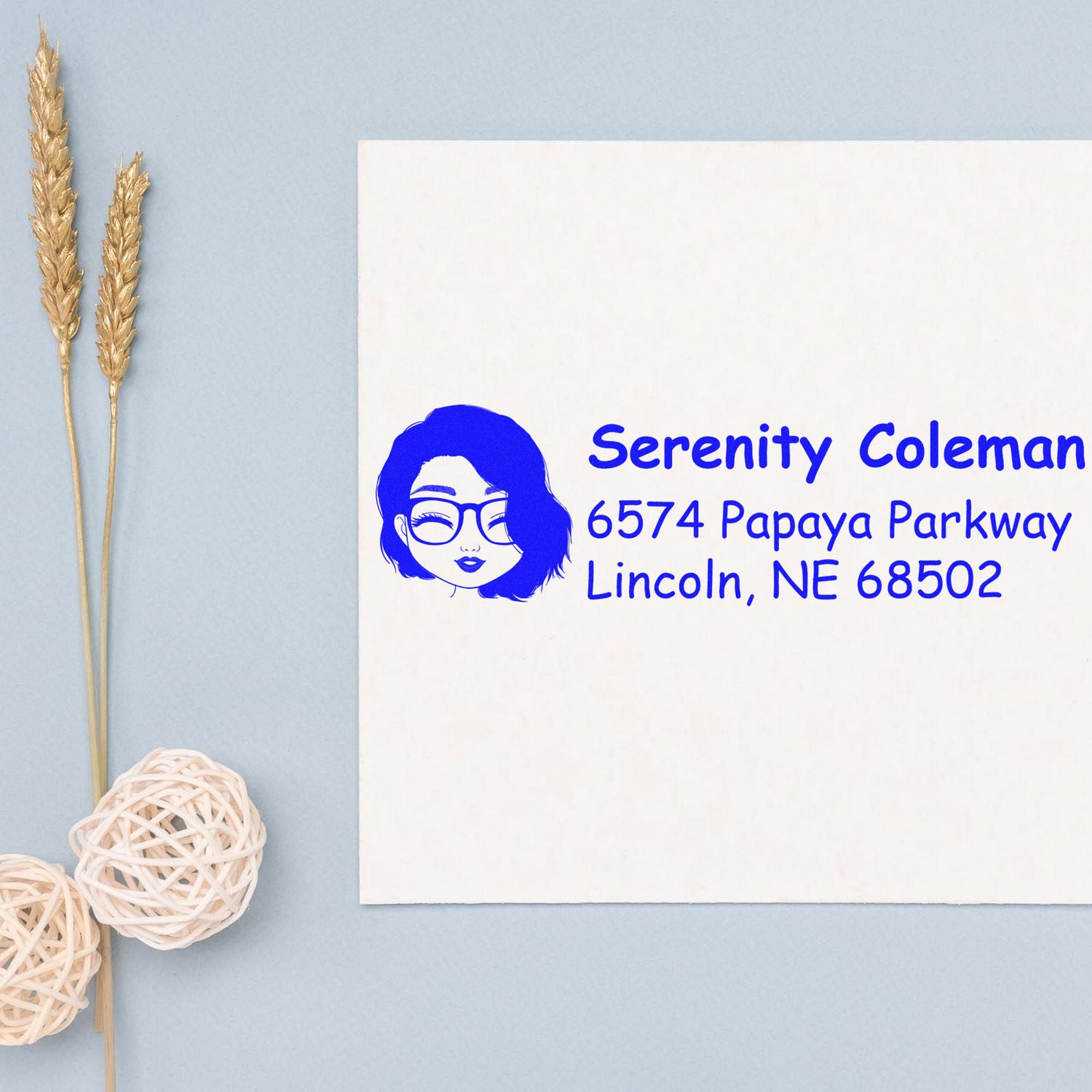 Blue custom address stamp seal with woman logo and Serenity Coleman address on white paper, on a light blue background.