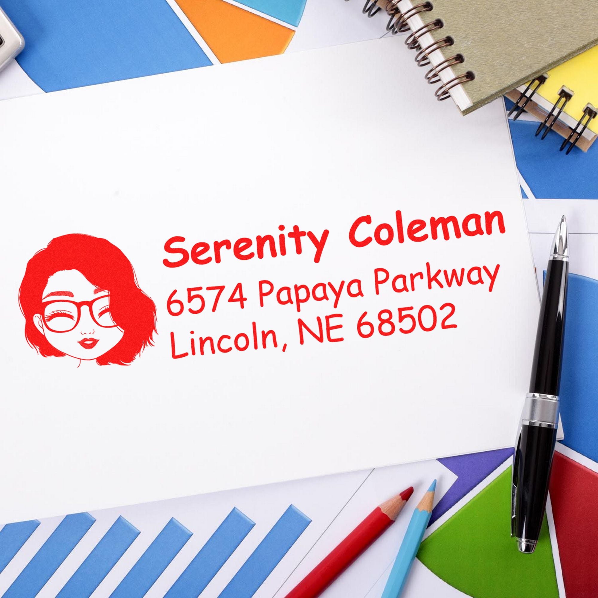 Red custom address stamp and seal on white envelope, surrounded by colorful stationery and pens.