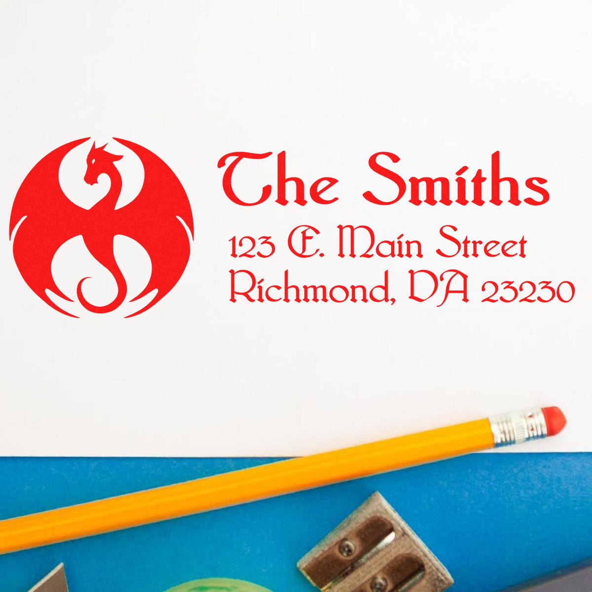 Red custom stamp and seal with dragon logo, The Smiths address text, on white paper beside a yellow pencil.