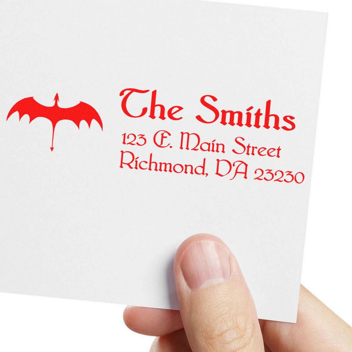 Red custom stamp and seal with bat logo and return address on white card, held by hand.