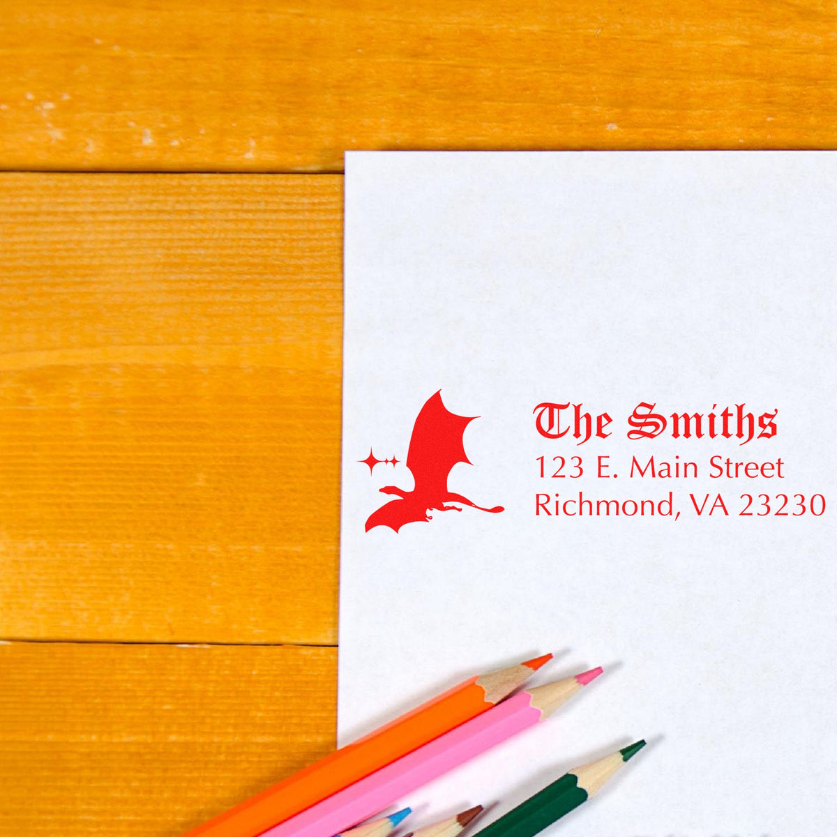 Custom red stamp and seal for The Smiths with address, on white paper beside colored pencils on a wood background.