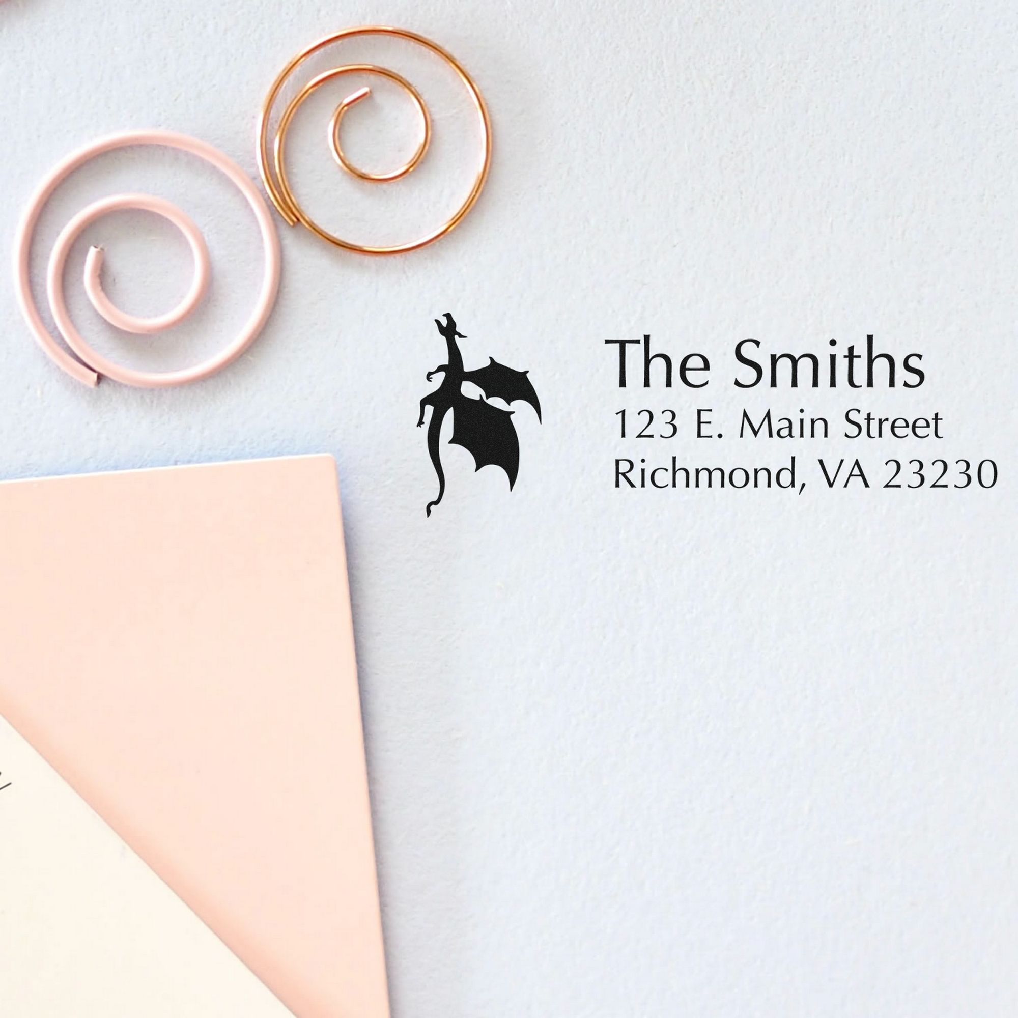 Custom stamp and wax seal branding on white paper, featuring rose gold and blush circles, black dragon emblem, and The Smiths address.