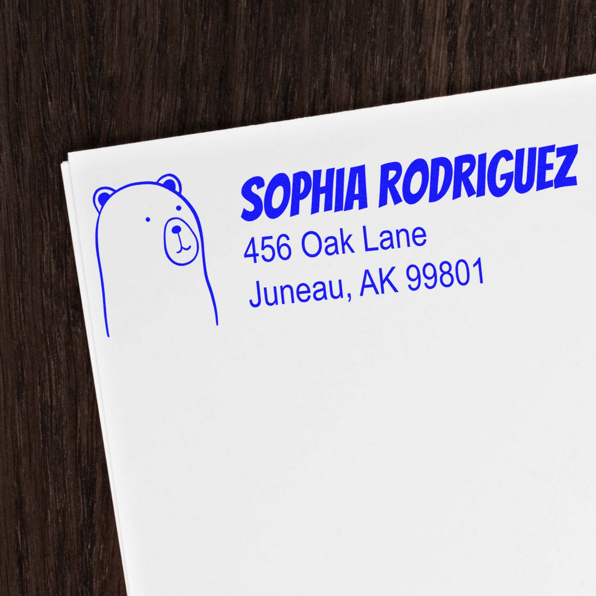 Cuddly Polar Bear Customize Mail Self-Inking Stamp on a white envelope with blue text reading "Sophia Rodriguez, 456 Oak Lane, Juneau, AK 99801." The custom stamp features a simple polar bear illustration on a dark wood background.
