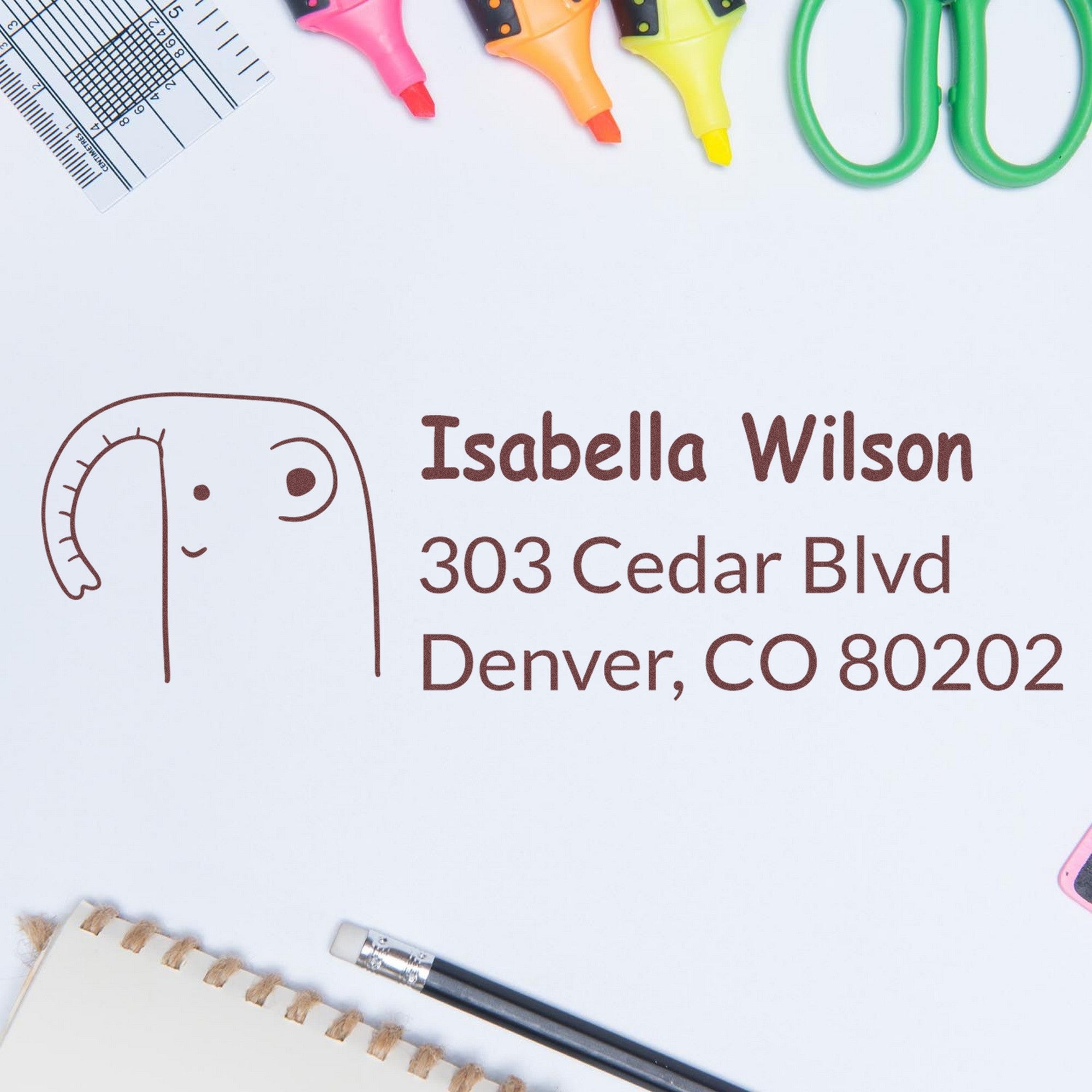 PSI Endearing Elephant Customized Address Label Pre-Inked Stamp featuring a cute elephant design with the text "Isabella Wilson, 303 Cedar Blvd, Denver, CO 80202" on a white background. Custom-Made New Address Stamp surrounded by colorful stationery items.