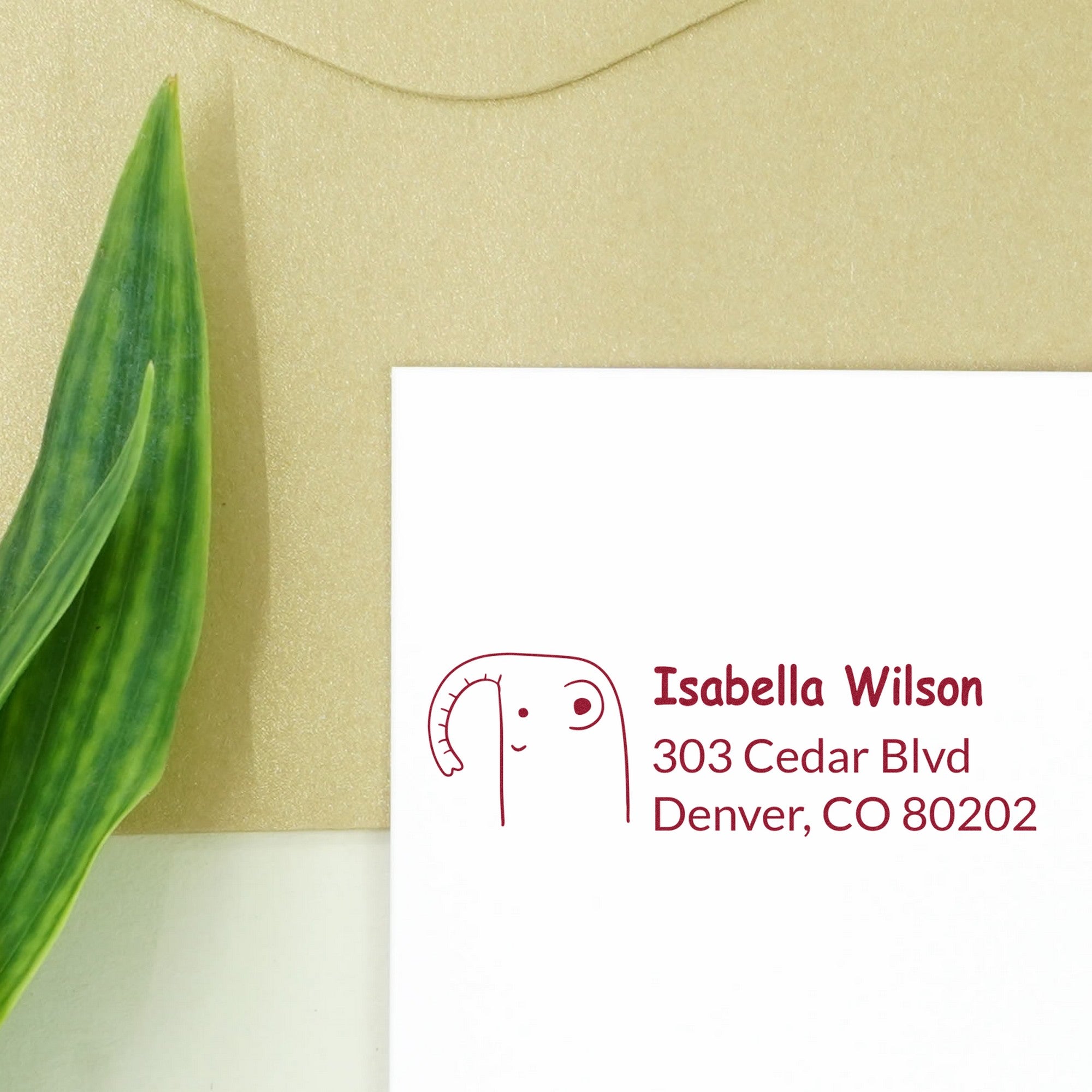 Slim Pre-Inked Endearing Elephant Custom Name and Address Stamp on a white envelope with green leaf. The Customized Return Mail Stamp features a cute elephant design and personalized address details in red ink.