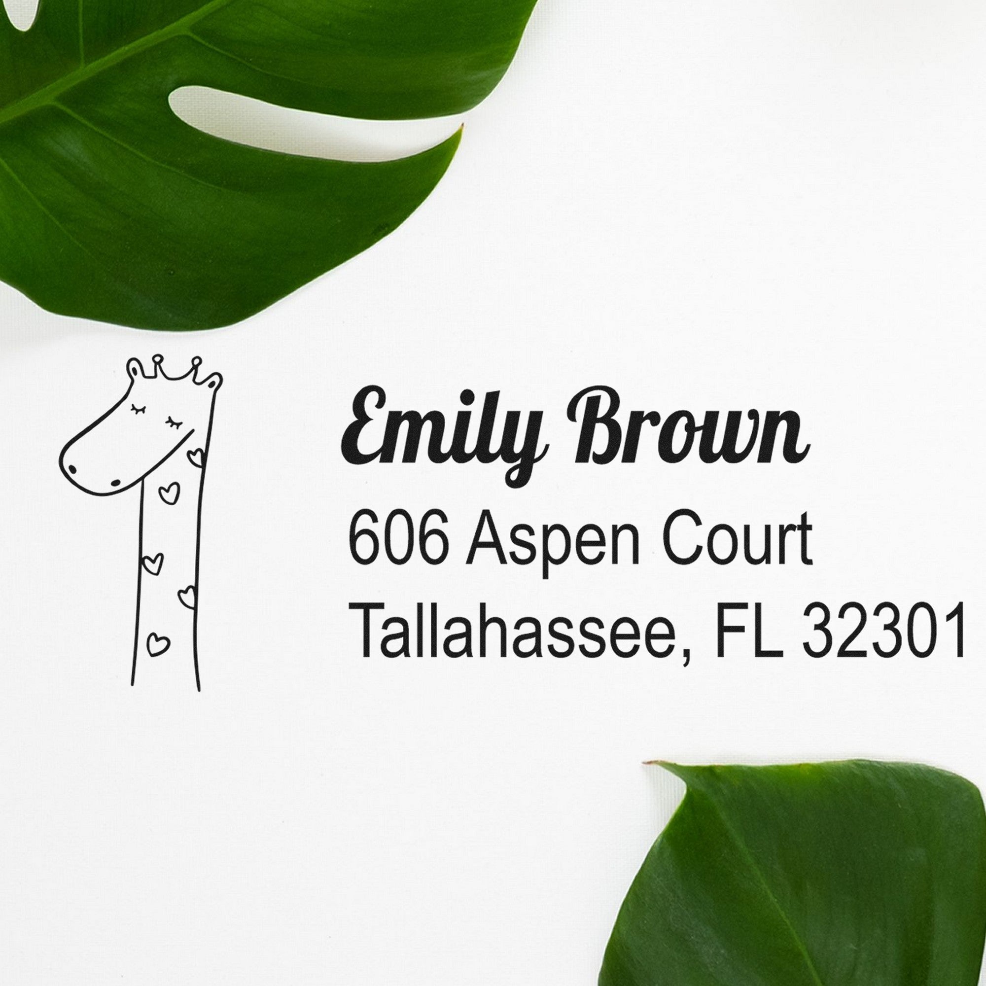 Lovely Giraffe Customize Address Label Self-Inking Stamp featuring a cute giraffe with hearts, alongside the text "Emily Brown, 606 Aspen Court, Tallahassee, FL 32301." Personalized Home Stamper on a white background with green leaves.