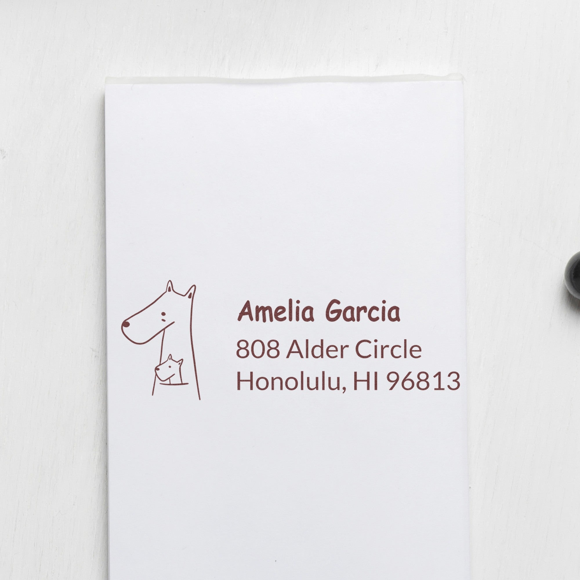Wood handle rubber stamp featuring a snuggly kangaroo design, used to personalize home addresses on envelopes. The customized address stamp displays "Amelia Garcia, 808 Alder Circle, Honolulu, HI 96813" in brown ink on a white envelope.