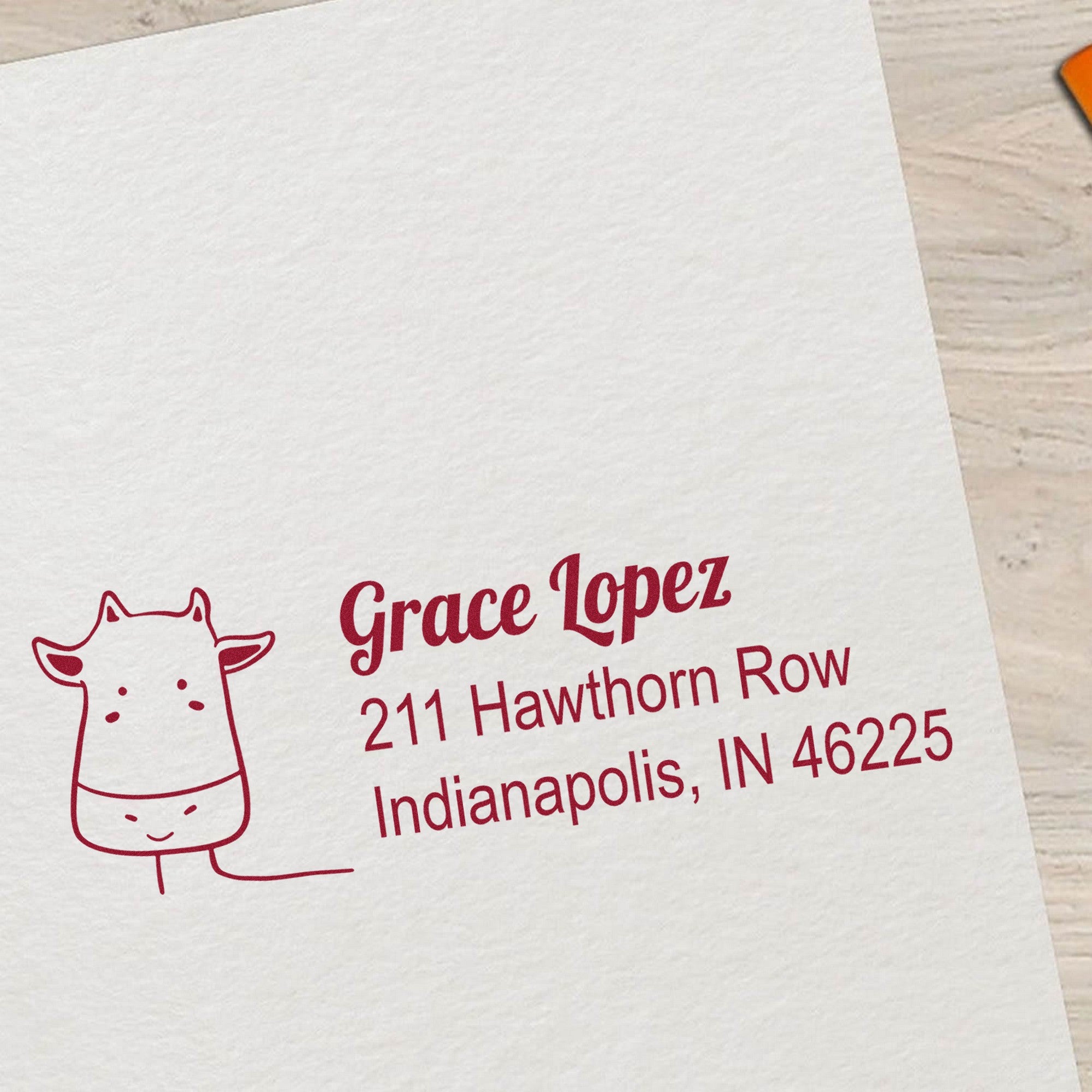 A custom-made mailing stamper with a PSI Cow Cuddles Handmade Mailing Address Pre-Inked Stamp design, featuring a cute cow illustration and the name "Grace Lopez" with an address in red ink on a white paper background.