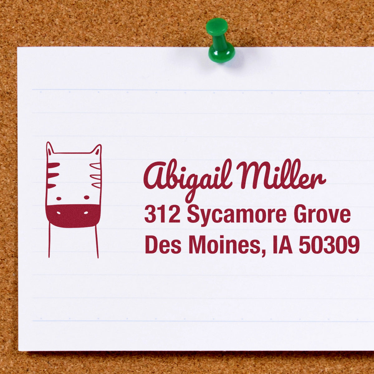 Image of a corkboard with a pinned note featuring a Slim Pre-Inked Frolicsome Zebra Custom Address Label Stamp. The stamp displays "Abigail Miller, 312 Sycamore Grove, Des Moines, IA 50309." This Customized New Address Stamp includes a playful zebra design.