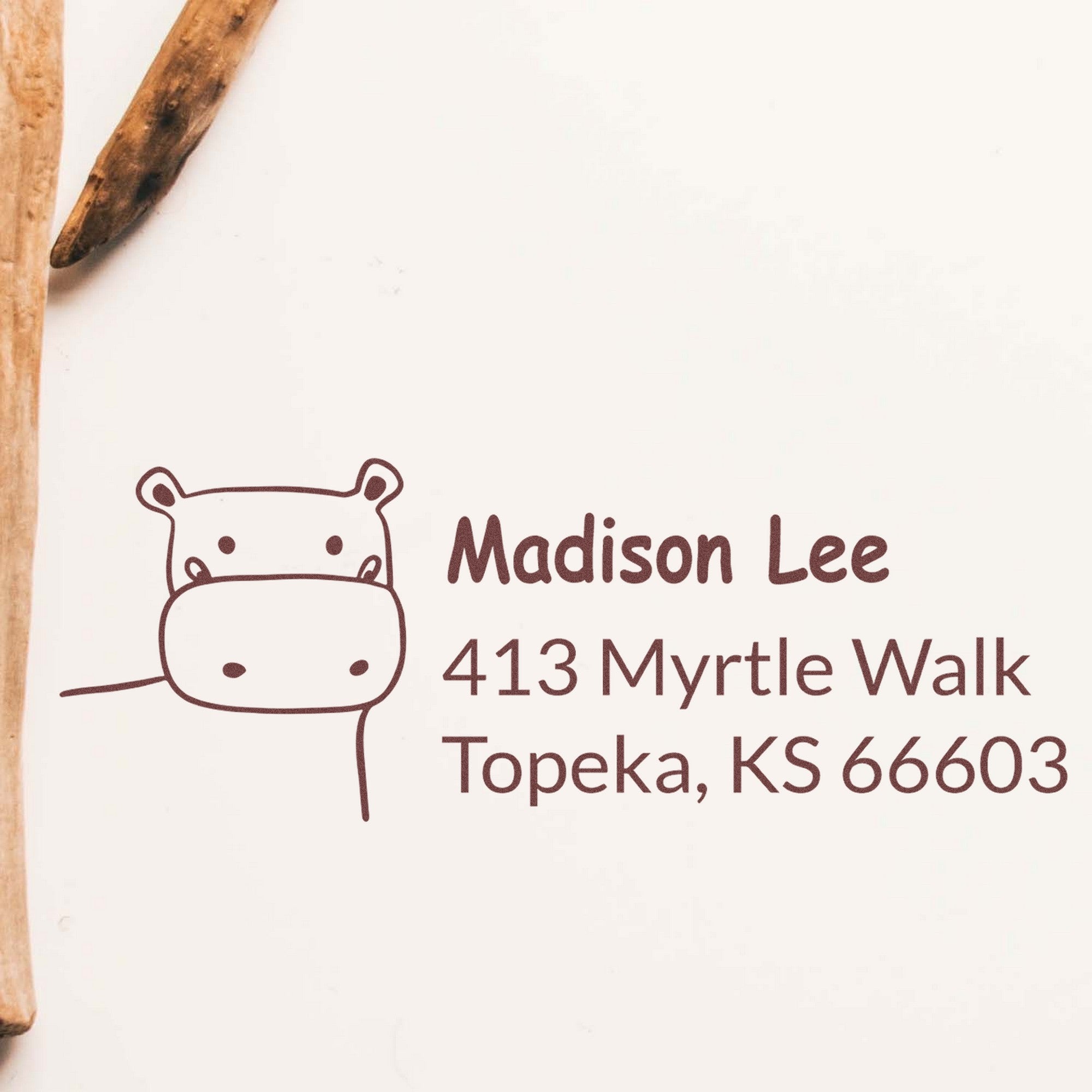 Wood Handle Happy Hippo Custom Mailing Rubber Stamp with a hippo design and the text "Madison Lee, 413 Myrtle Walk, Topeka, KS 66603." This Custom Return Mail Stamp is shown on white paper with a wooden handle visible on the side.