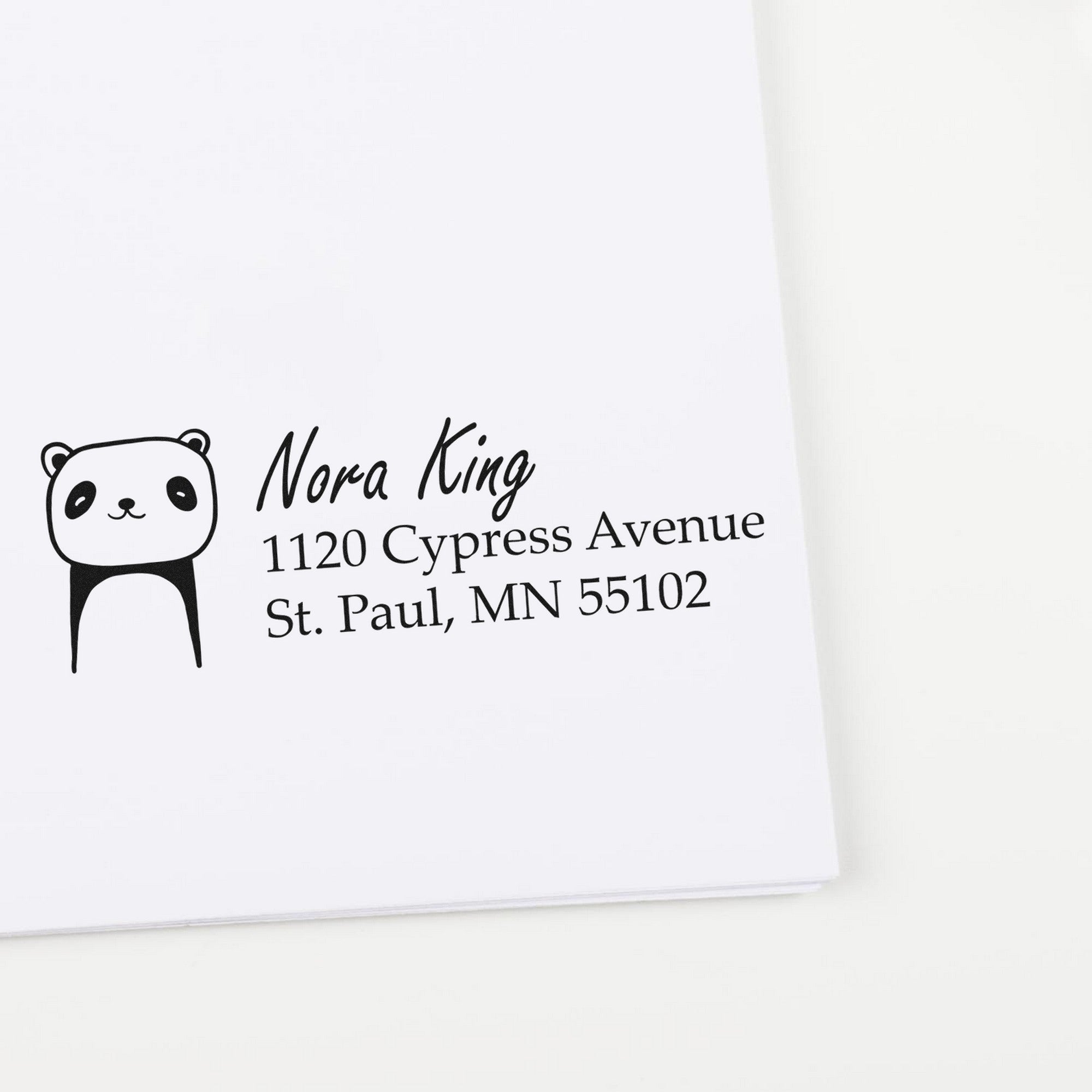 Image of a customized return mail stamp featuring a playful panda design with a wood handle. The stamp displays a home address for envelopes, reading "Nora King, 1120 Cypress Avenue, St. Paul, MN 55102."