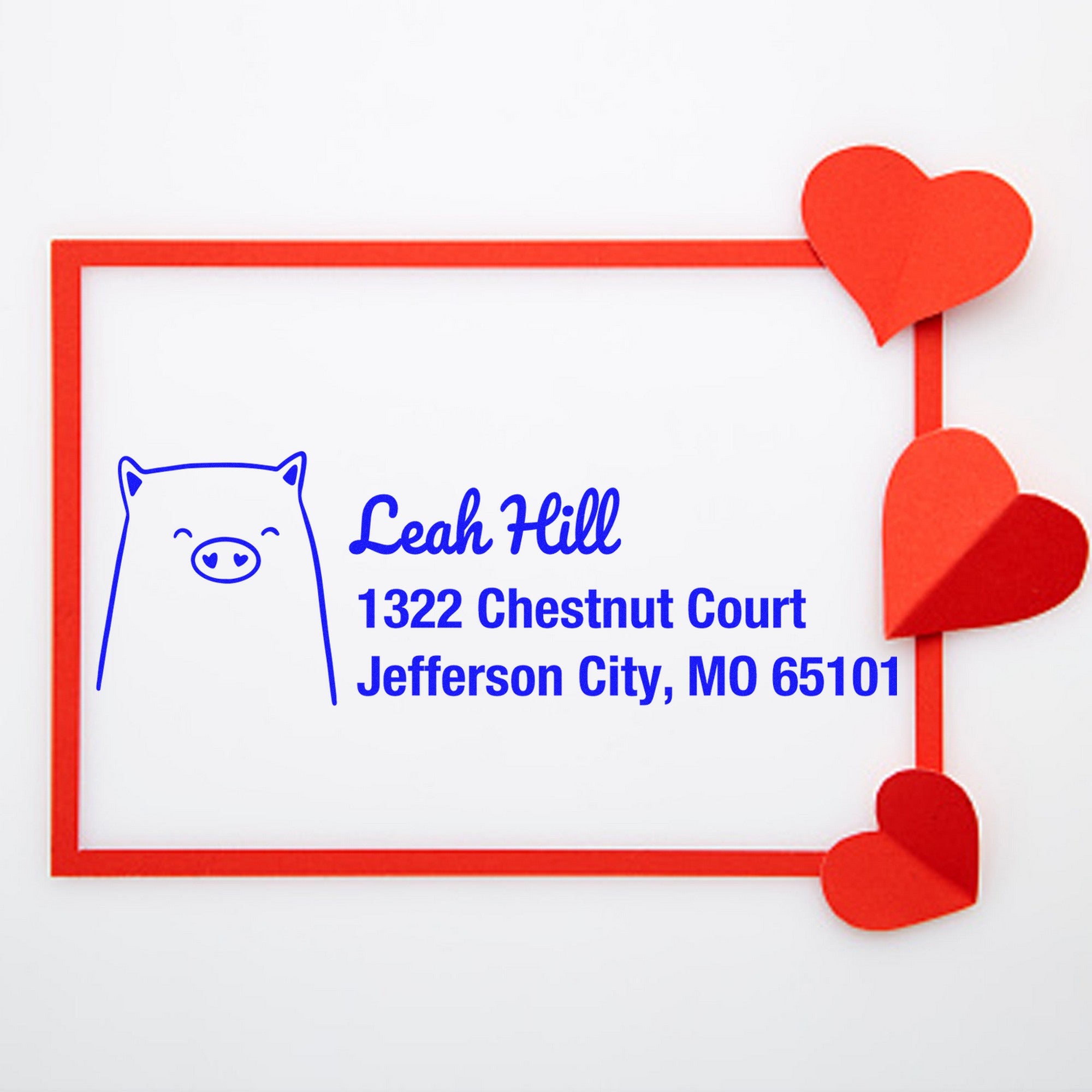Cheery Pig Personalized Mailing Self-Inking Stamp on a white background with a red heart frame. The custom stamp features a pig illustration and text: "Leah Hill, 1322 Chestnut Court, Jefferson City, MO 65101" in blue.