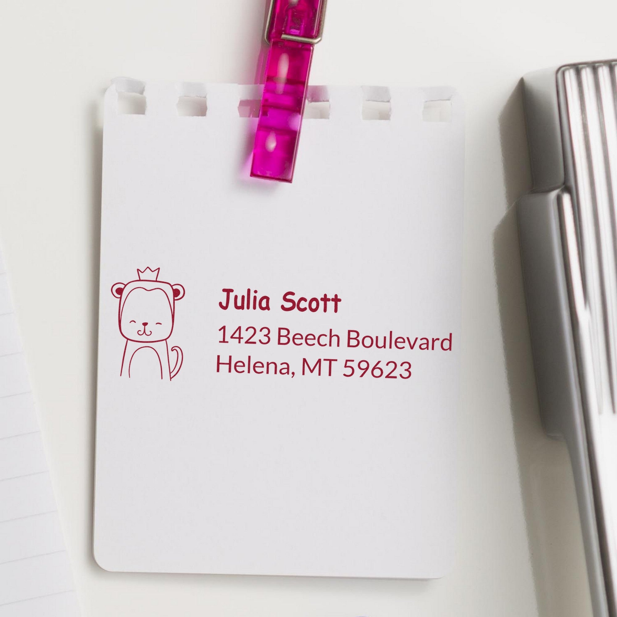 Image of a notepad with a red stamp featuring a mischievous monkey design and the text "Julia Scott, 1423 Beech Boulevard, Helena, MT 59623." The stamp is a wood handle customized return address rubber stamp, also known as a customized home stamp.