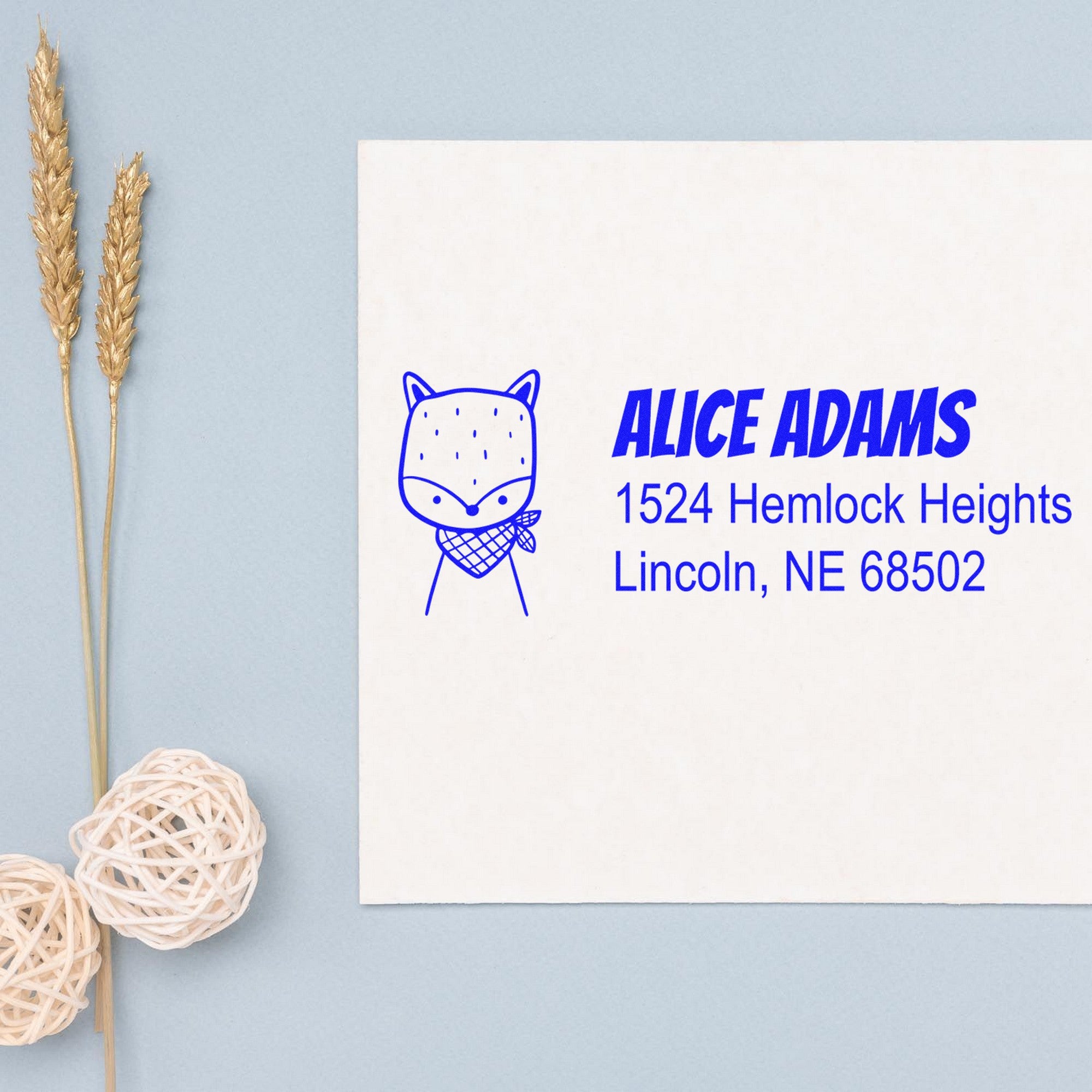 Image of a personalized address stamper with a wood handle, featuring a fancy fox design. The stamp displays the name "Alice Adams" and address "1524 Hemlock Heights, Lincoln, NE 68502" in blue ink on a white card.