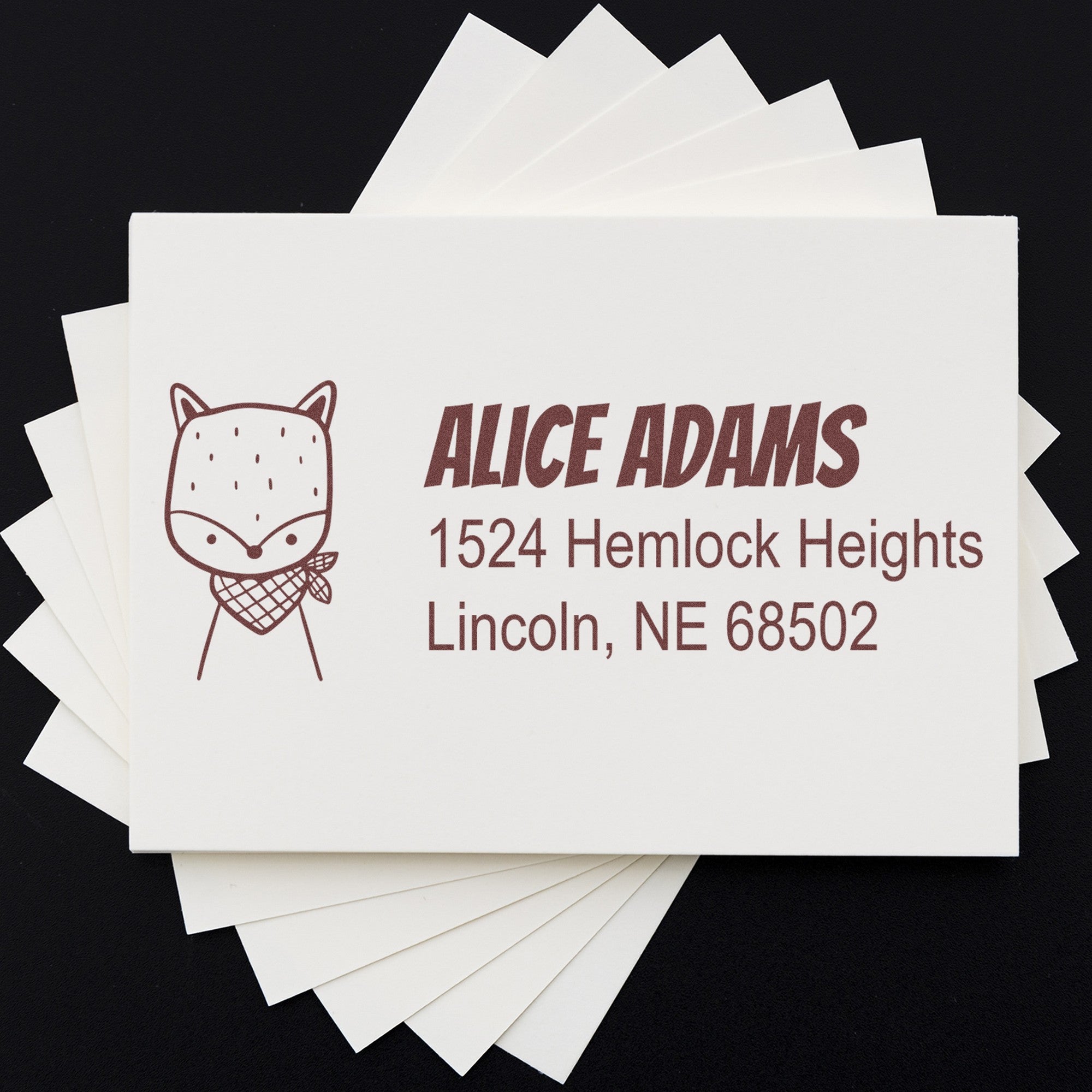 Wood handle fancy fox customized name and address rubber stamp on cards, featuring a personalized new address stamp with a cute fox illustration and the text "Alice Adams, 1524 Hemlock Heights, Lincoln, NE 68502" in brown ink.