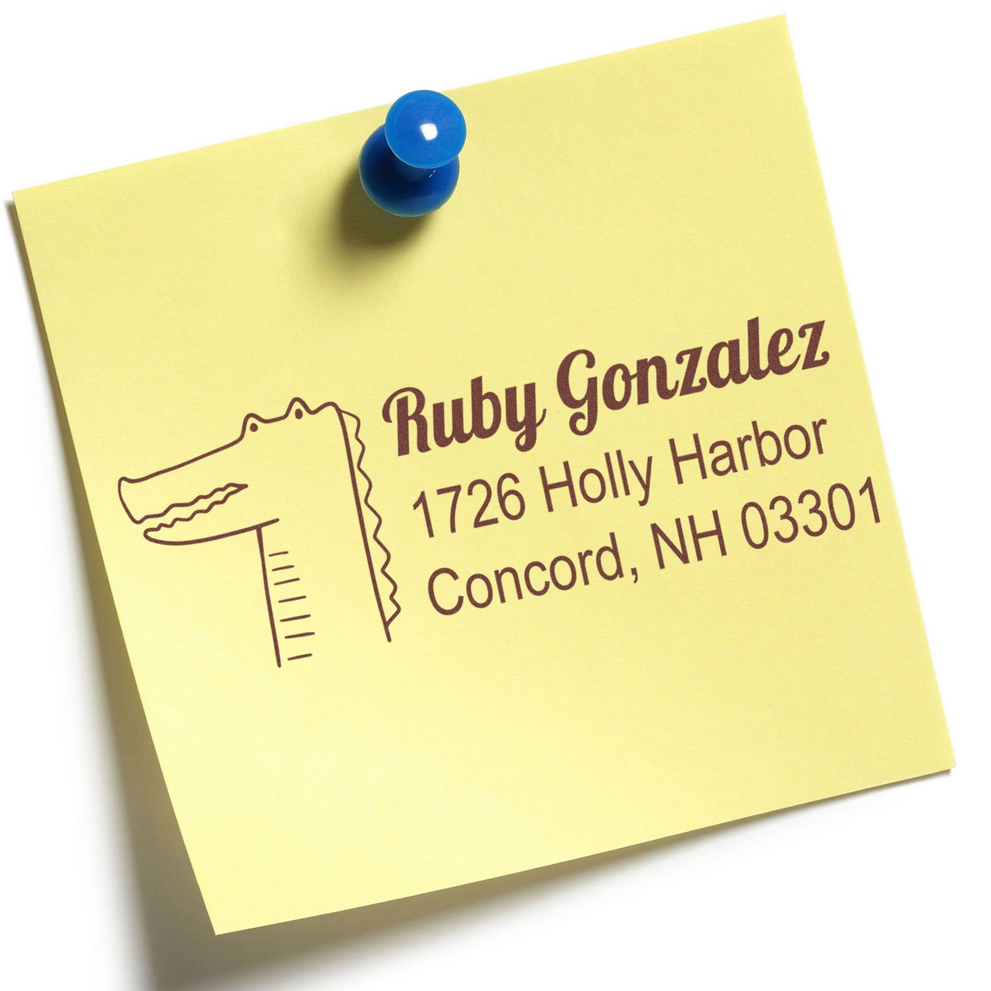 Yellow sticky note with a blue pushpin featuring a PSI Bright Eyed Crocodile design. Text reads "Ruby Gonzalez, 1726 Holly Harbor, Concord, NH 03301." This Custom-Made New Address Stamp is ideal for personalizing envelopes.
