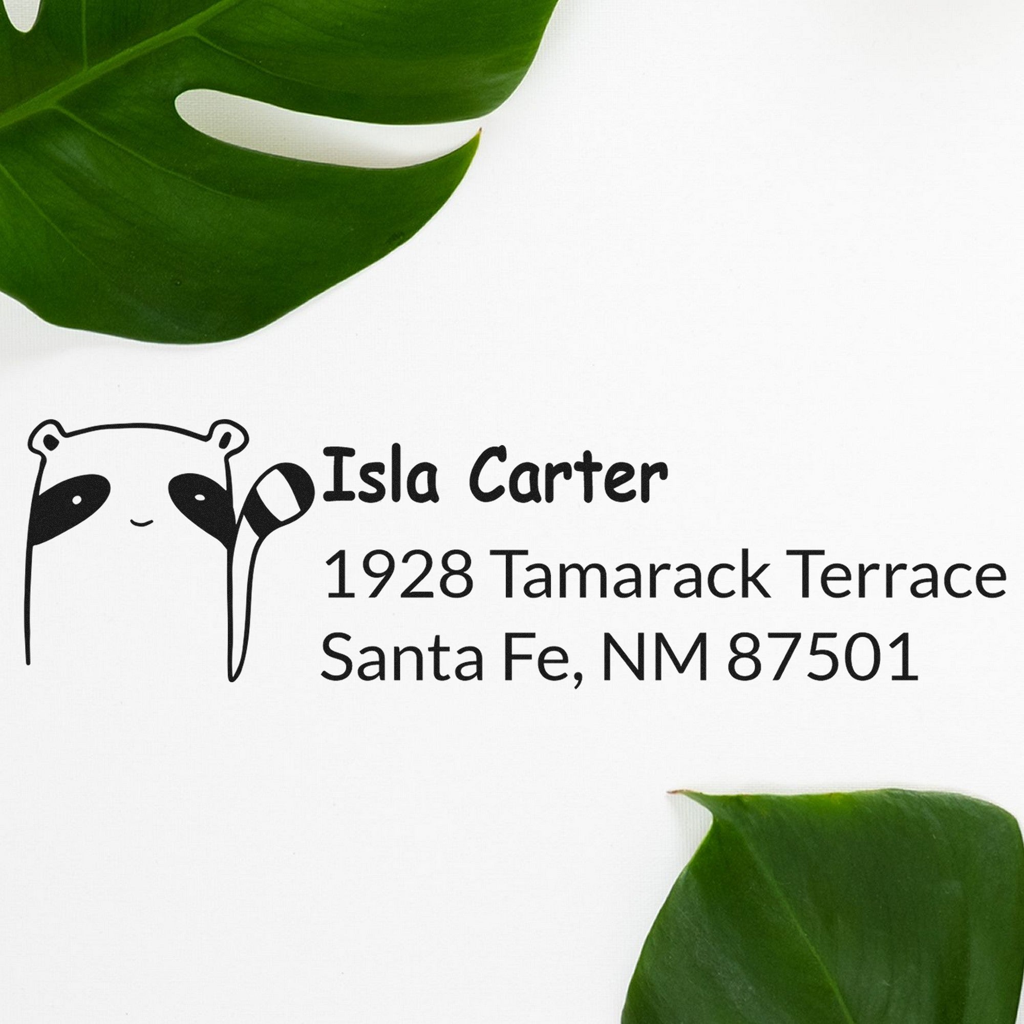 PSI Renegade Racoon Customizable Address Pre-Inked Stamp featuring a raccoon design with text 'Isla Carter, 1928 Tamarack Terrace, Santa Fe, NM 87501'. Custom Home Stamper displayed on a white background with green leaves.