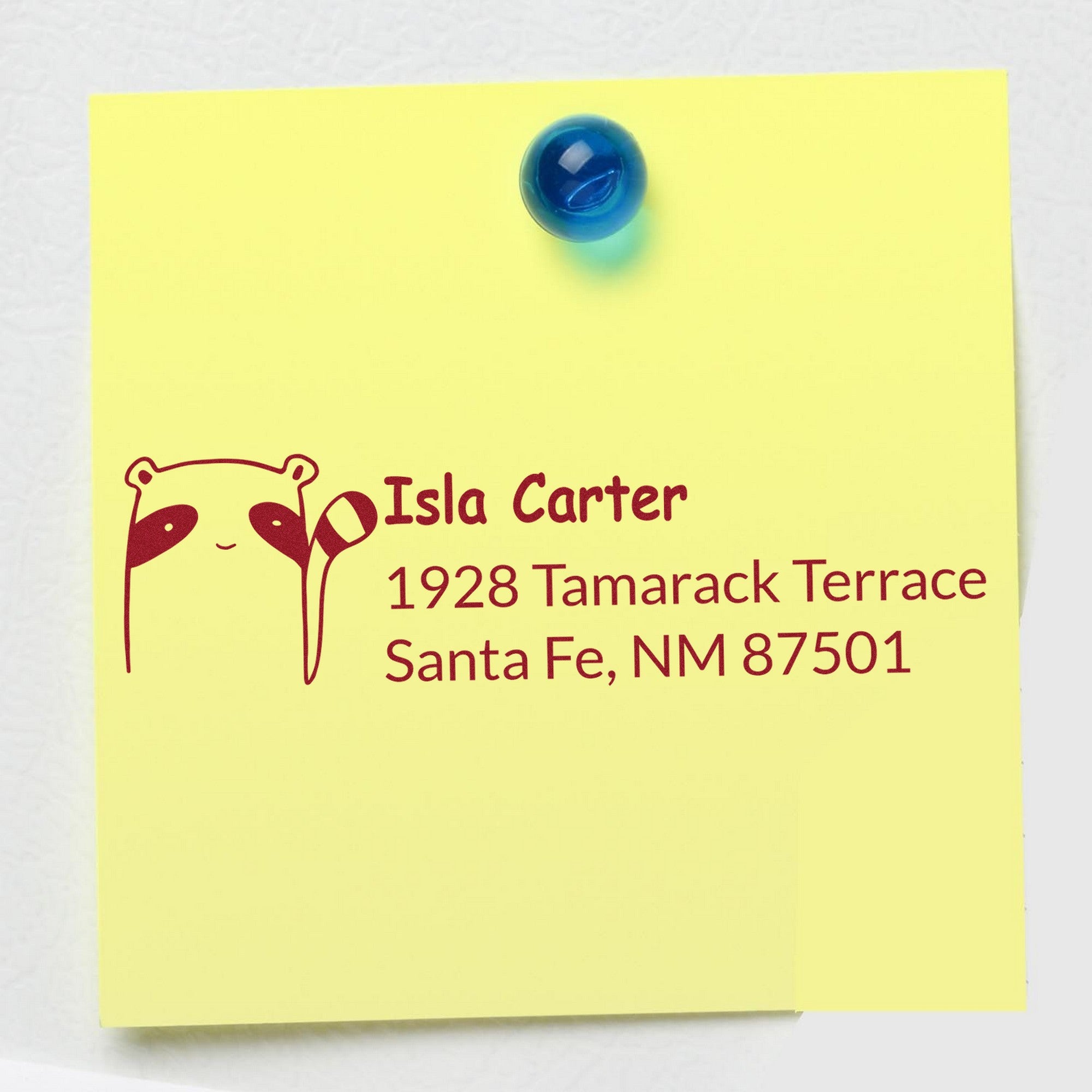 Wood Handle Renegade Racoon Customized Address Return Rubber Stamp on a yellow note with text: "Isla Carter, 1928 Tamarack Terrace, Santa Fe, NM 87501." Blue magnet holds the note. Custom Home Stamper design with raccoon graphic.