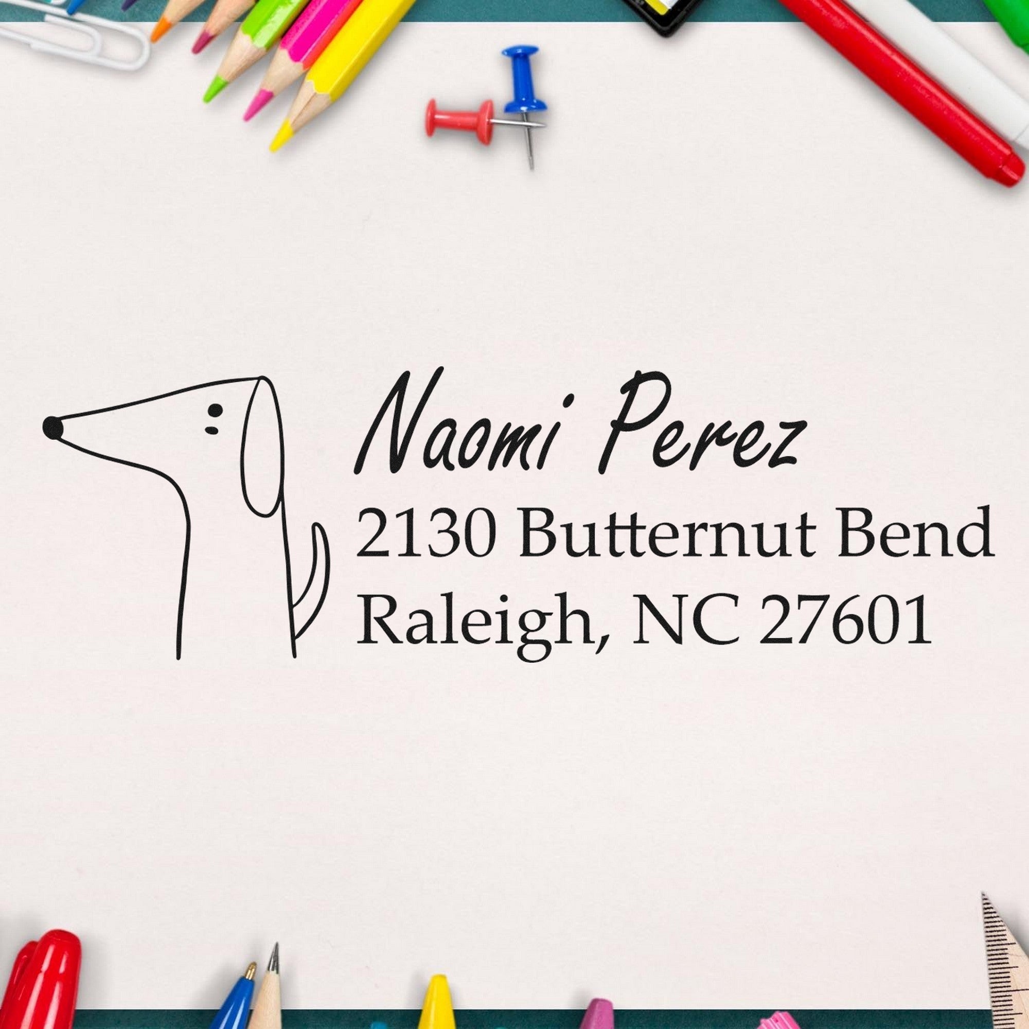 PSI Delightful Dog Customizable Name and Address Pre-Inked Stamp displayed on paper with "Naomi Perez, 2130 Butternut Bend, Raleigh, NC 27601." Surrounded by colorful stationery, this Custom Return Mail Stamp features a simple dog illustration.