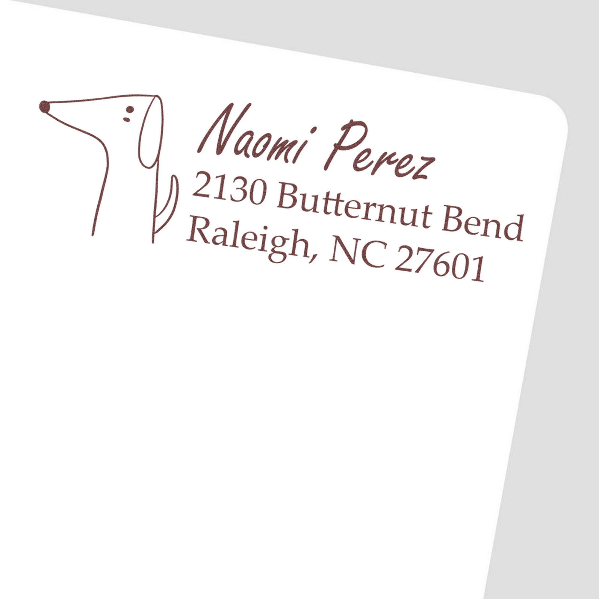 Image of a customized address stamp featuring a delightful dog illustration and the text "Naomi Perez, 2130 Butternut Bend, Raleigh, NC 27601." The stamp has a wood handle, ideal for personalized mail. Keywords: Wood Handle Delightful Dog Customized Mail Address Rubber Stamp, Customized Address Stamp.