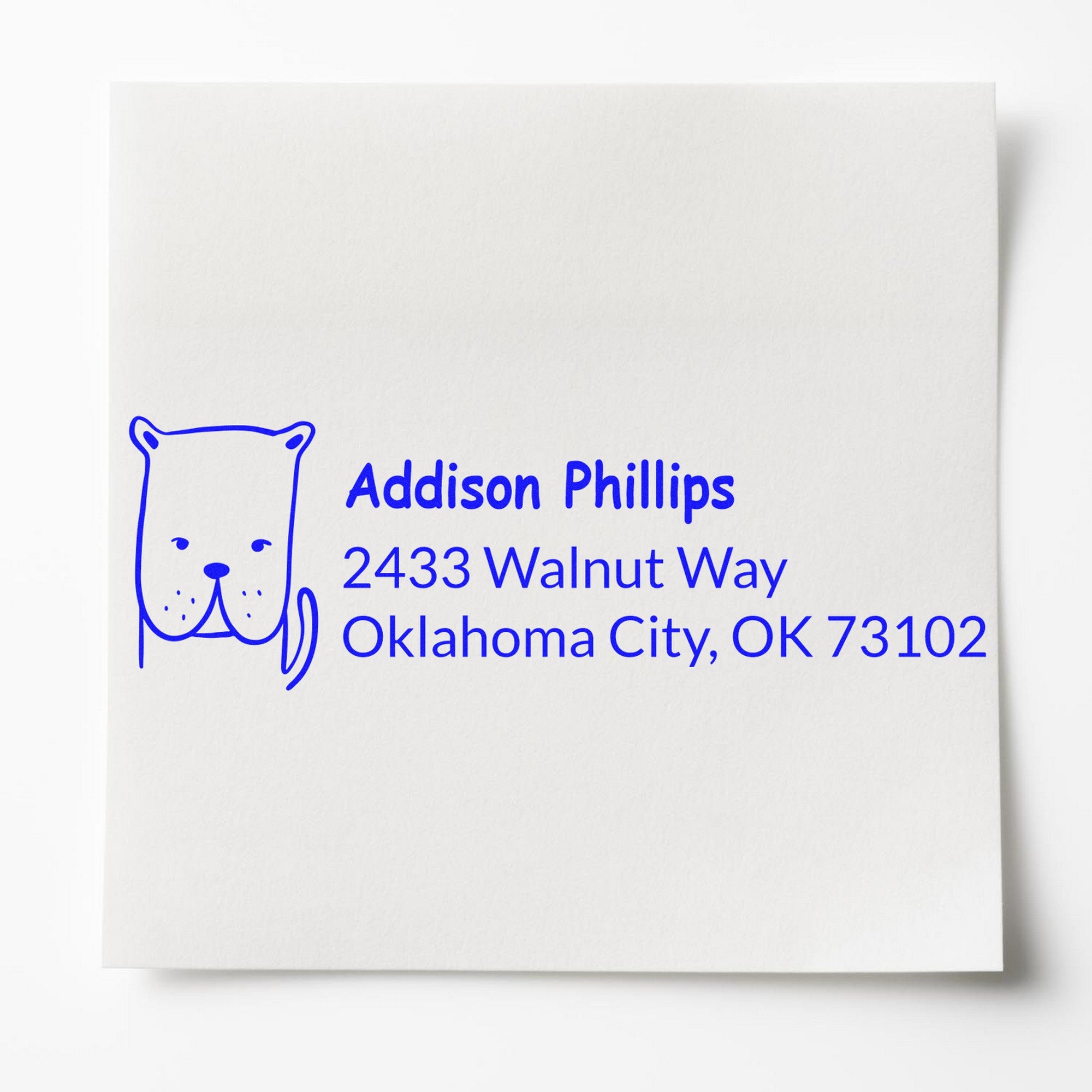 Daring Dog Custom Name and Address Self-Inking Stamp featuring a blue dog illustration and text "Addison Phillips, 2433 Walnut Way, Oklahoma City, OK 73102." Ideal for a Customized Return Mail Stamper on white paper.