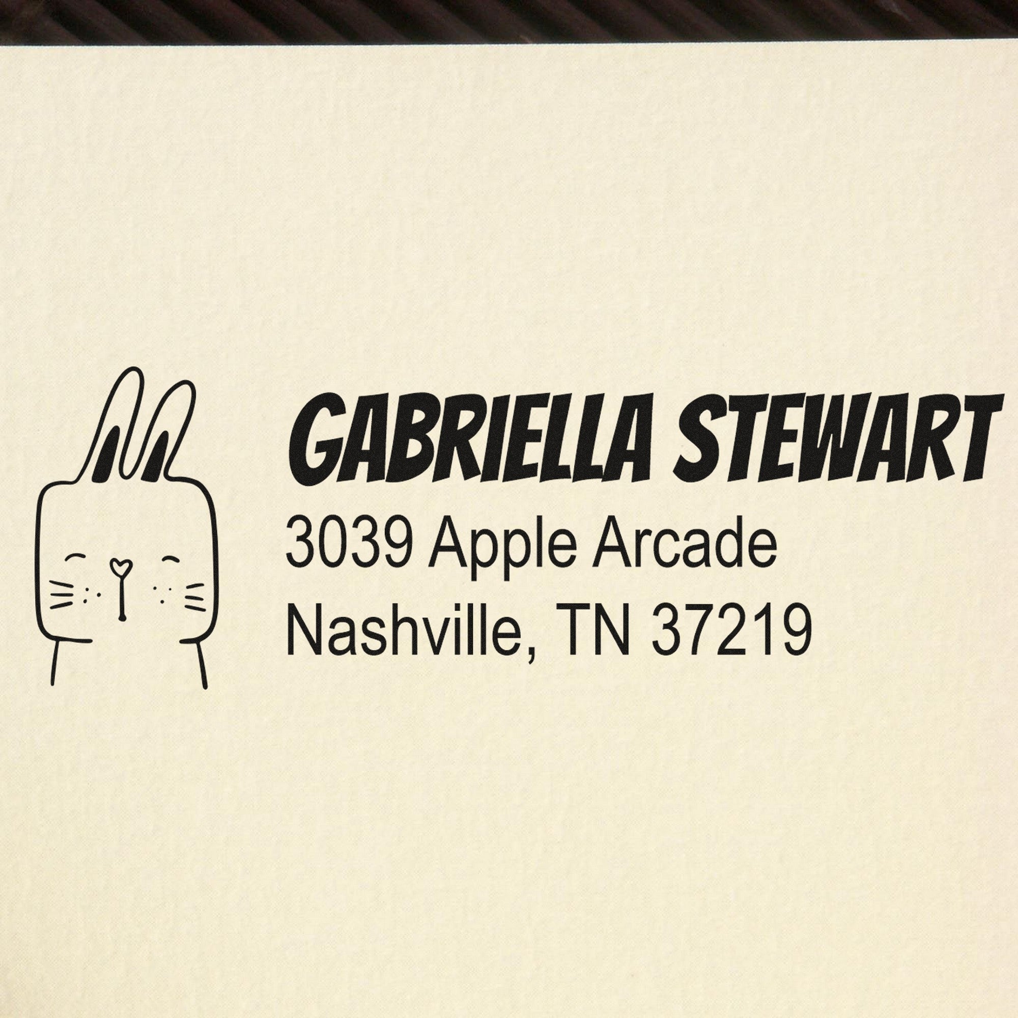 Wood Handle Fuzzy Rabbit Handmade Home Address Rubber Stamp featuring a cute rabbit design. Customizable Address Stamp with the name "Gabriella Stewart" and address "3039 Apple Arcade, Nashville, TN 37219" printed on a beige surface.