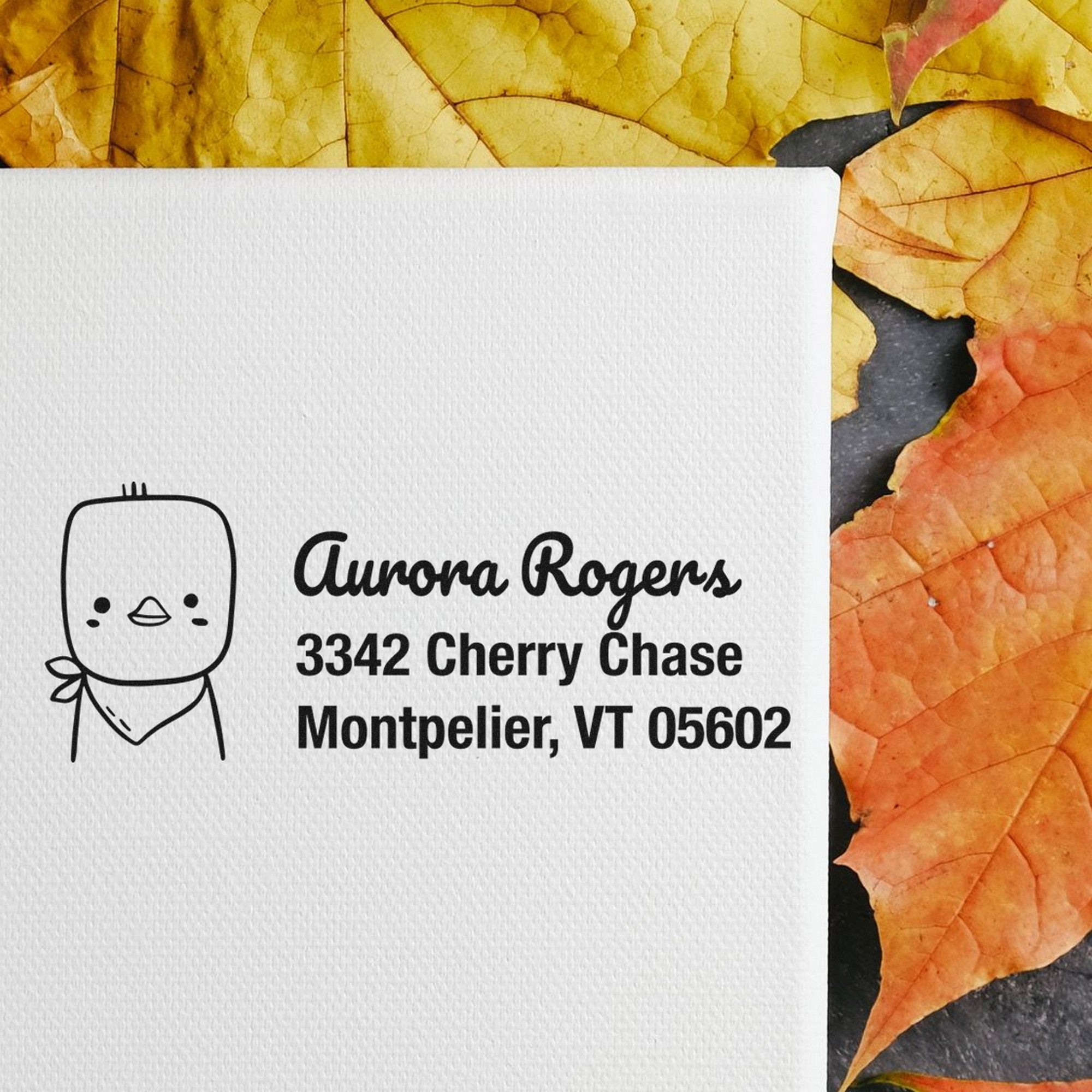 Wood handle cute chick handmade mail address rubber stamp on white paper with "Aurora Rogers, 3342 Cherry Chase, Montpelier, VT 05602" text. Customizable address stamp displayed on a background of autumn leaves.