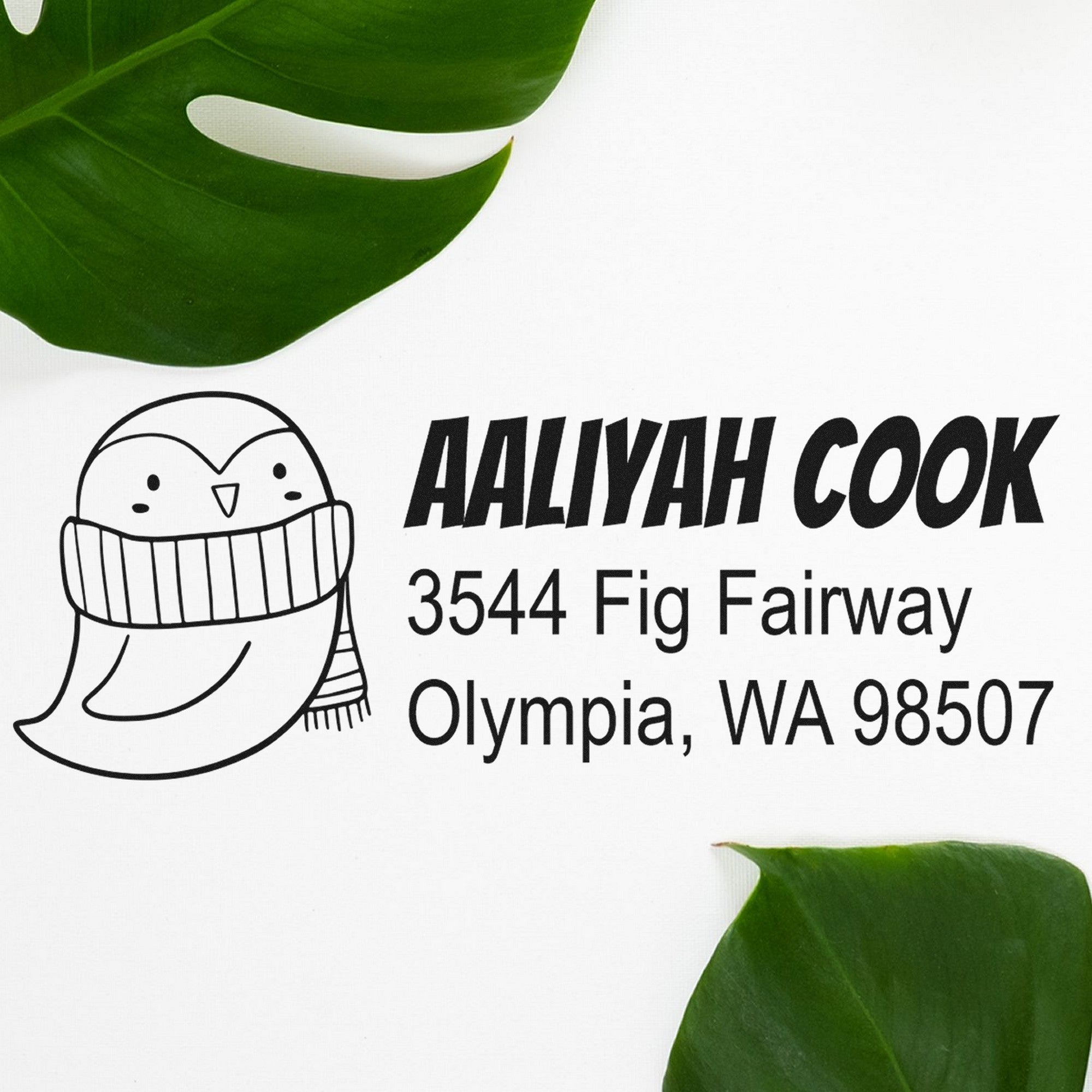 Wood handle pretty penguin handmade home address rubber stamp featuring a cute penguin in a scarf. Custom new address stamp with the name "Aaliyah Cook" and address "3544 Fig Fairway, Olympia, WA 98507" on a white background with green leaves.